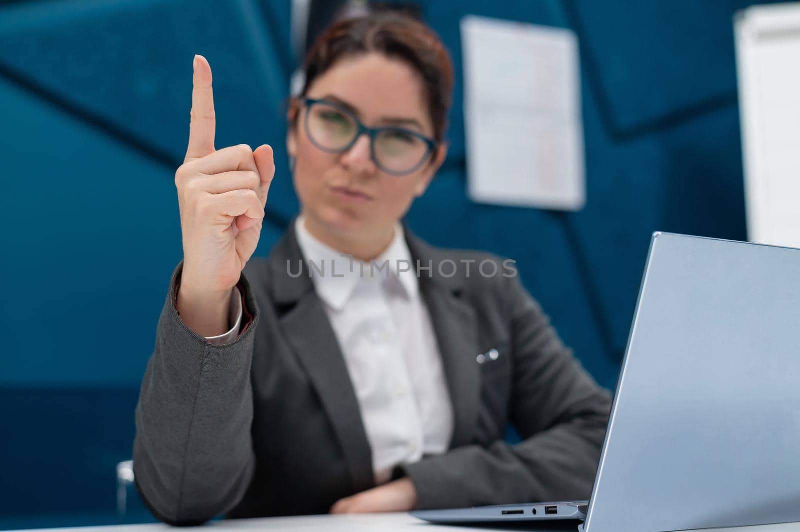 Angry business woman is sitting at her desk and pointing her finger