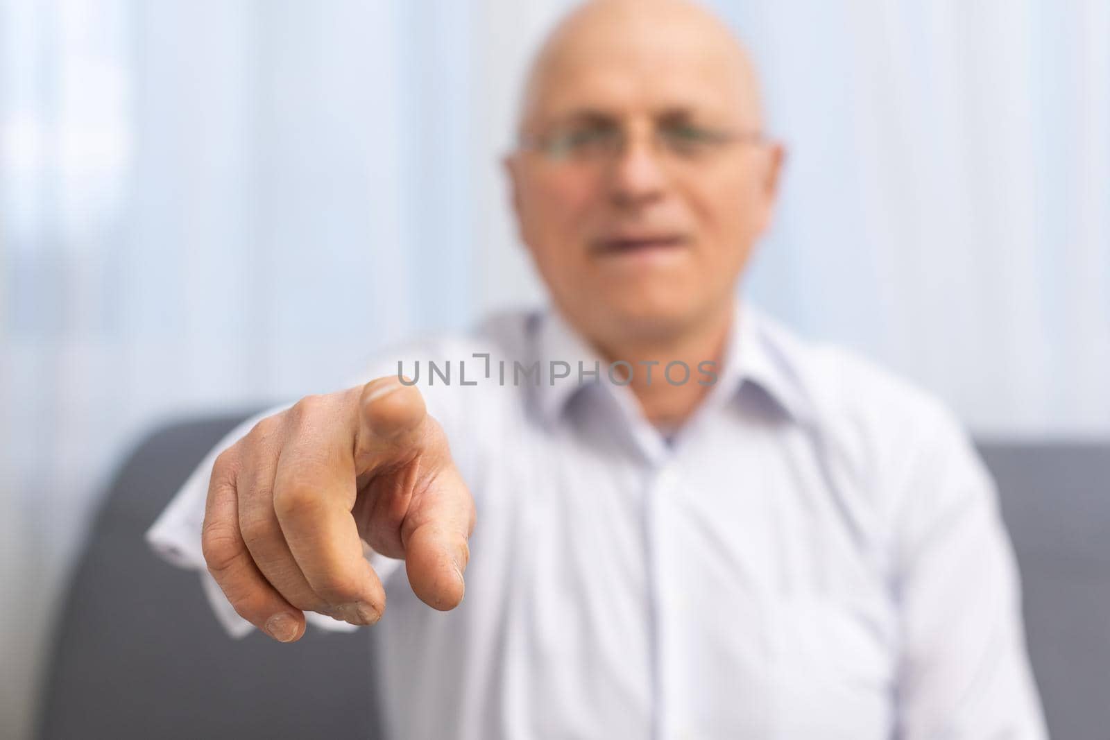 Mature man pointing with his finger at you on grey background.