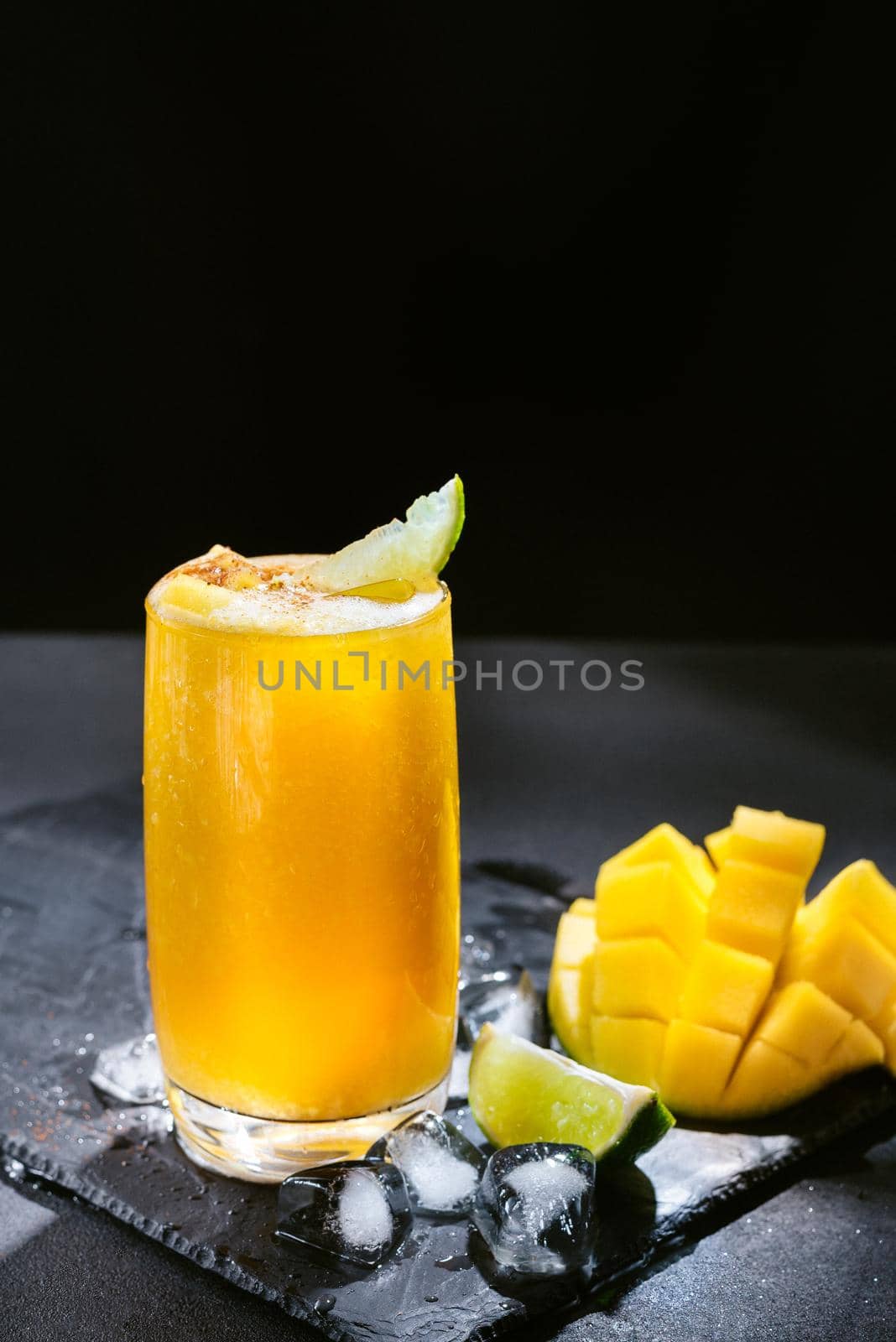 Mango juice on a dark background. Summer drink with ice and slices of mango and lime