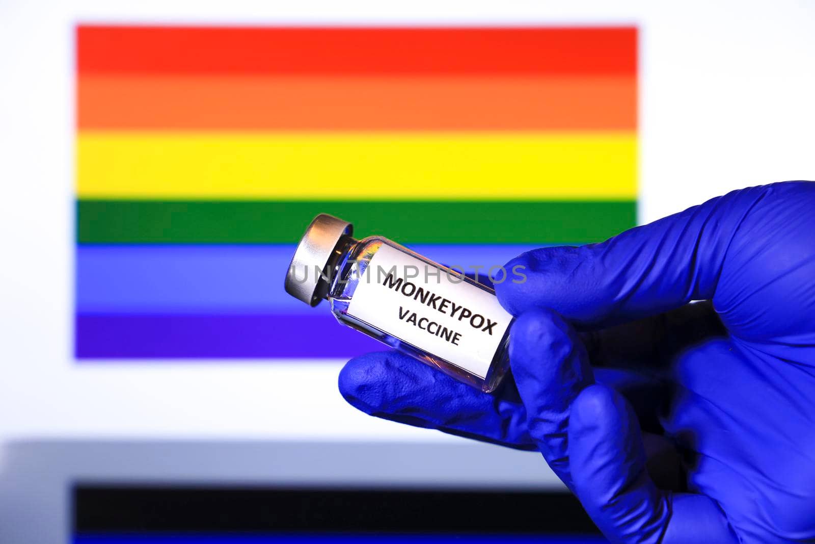 Hand holding vial with monkeypox vaccine. Rainbow flag in the background.