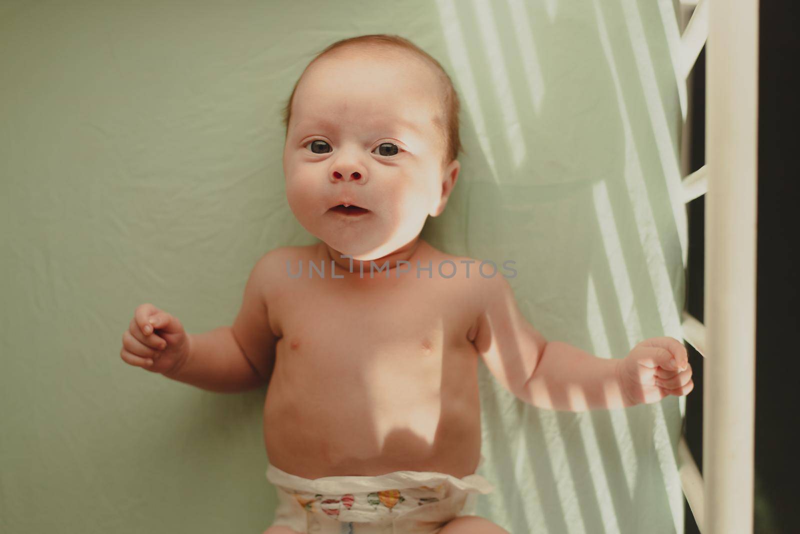 The baby is lying in his crib and looking at the camera . A happy child. Children's article. Copy Space
