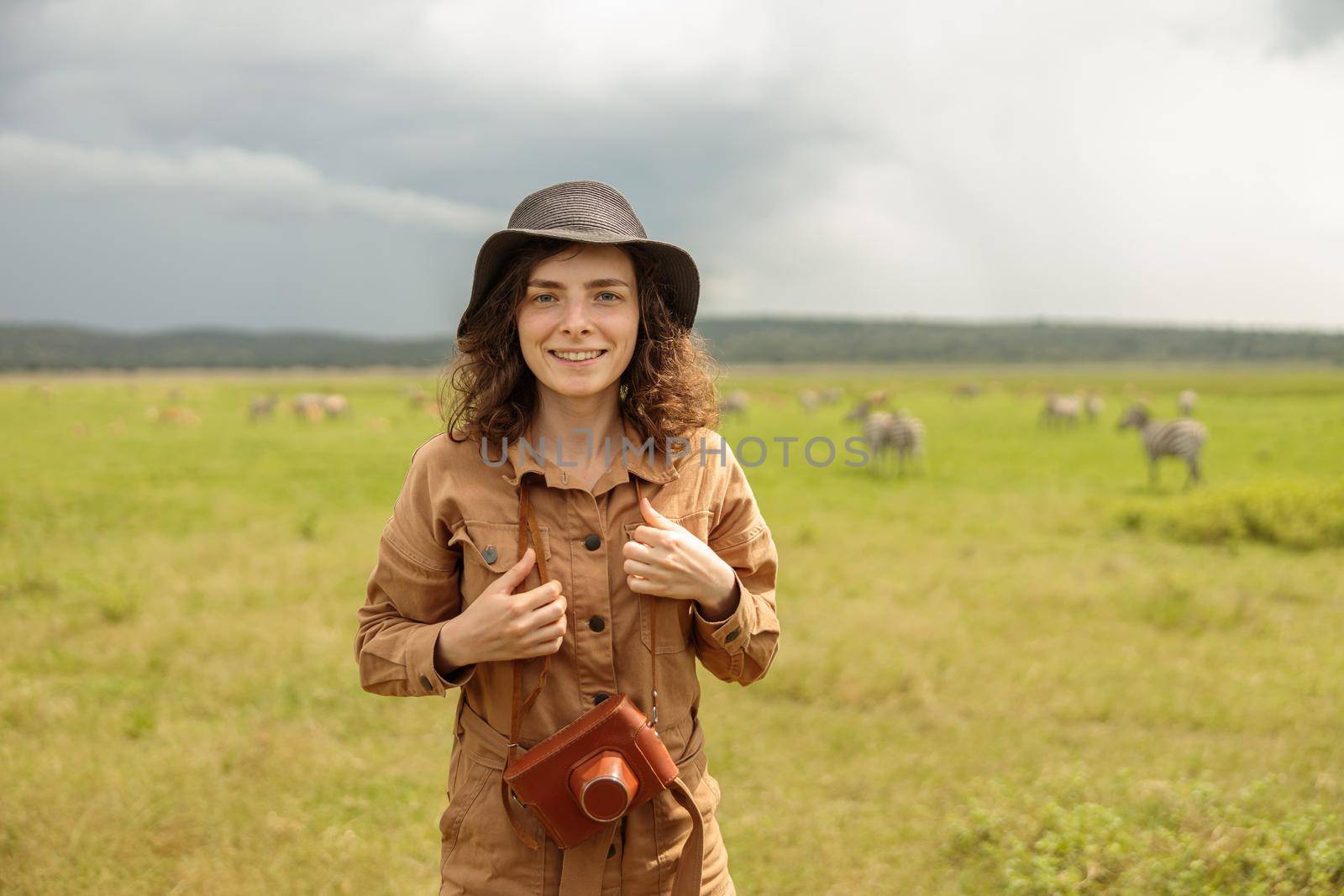 Smiling lady in hat standing in a national park in Africa with wild animals in the background