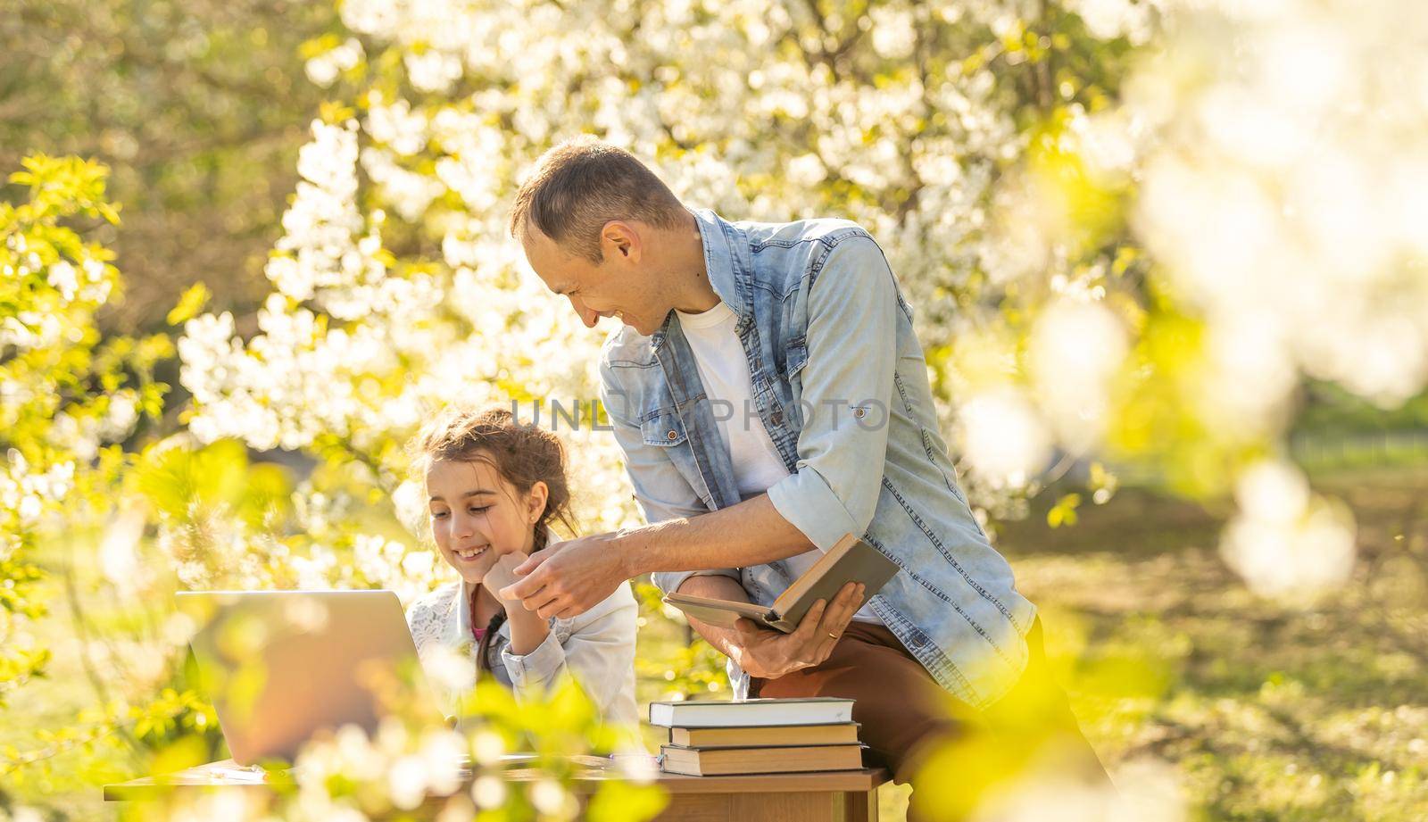 Caring young father helps little daughter, studying together watch online lesson on laptop, attentive dad and small girl child learning at home, have web class on computer on quarantine. outdoor by Andelov13