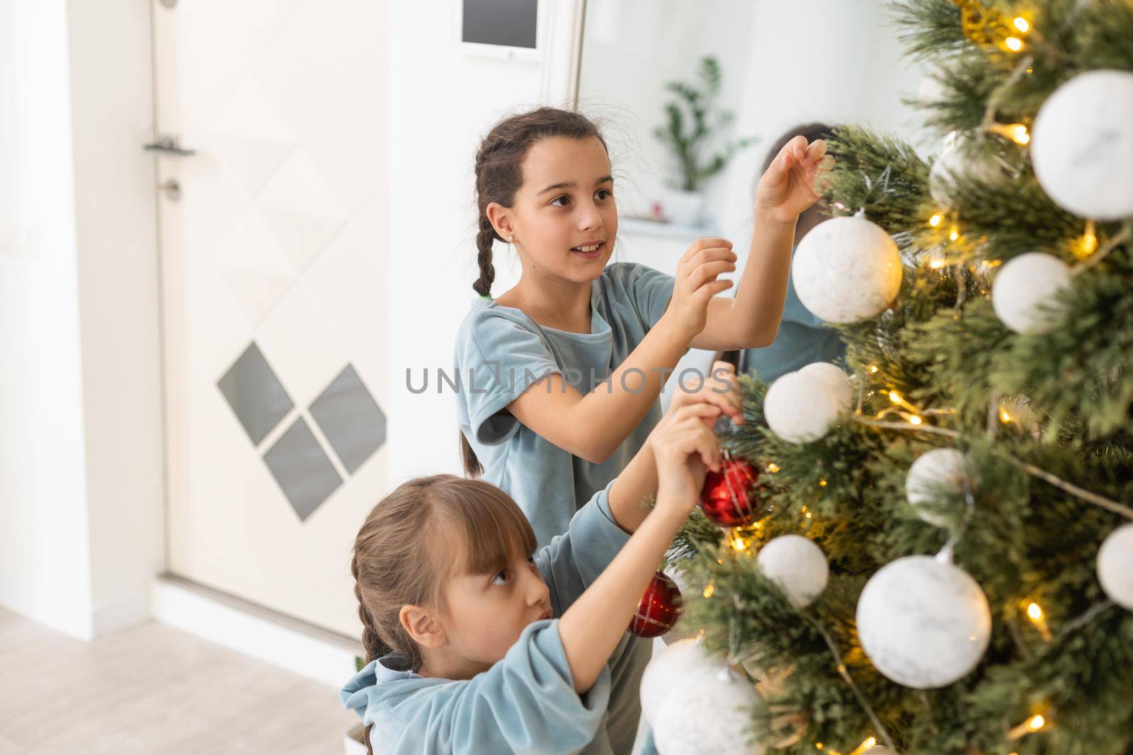 christmas, x-mas, winter, happiness concept - two adorable girls playing near the Christmas tree.