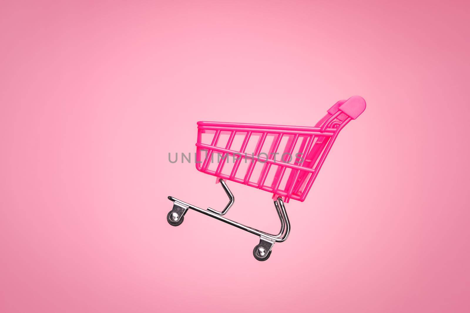 Pink shopping trolley supermarket concept. Empty trolley cart isolated pink background. Sale cart shop online marketplace. Toy pink concept sales online shopping cart supermarket sales shopping symbol by synel