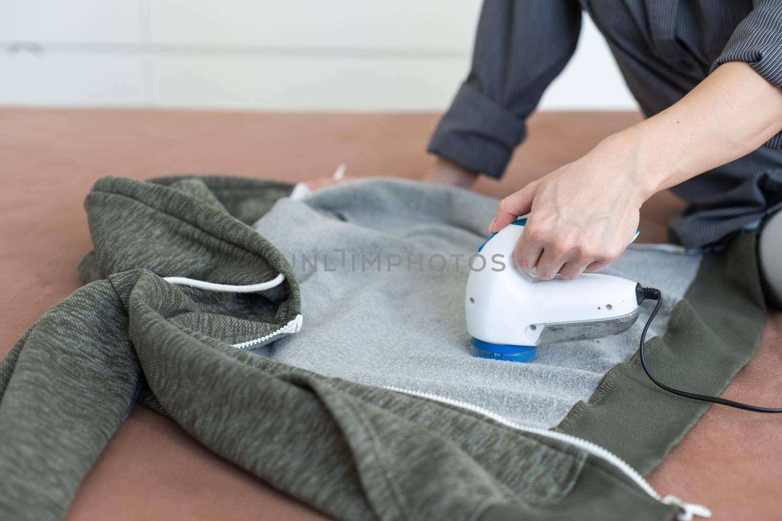 Wireless device for cleaning knitted fabrics from lint. The woman is removing the lint from the sweater