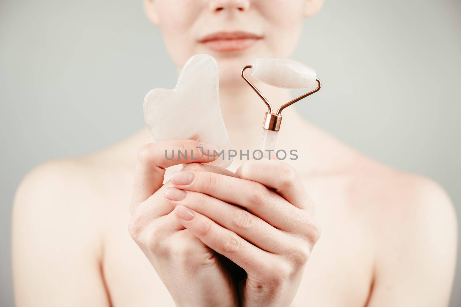 Caucasian woman holding pink roller massager and gouache scraper on white background