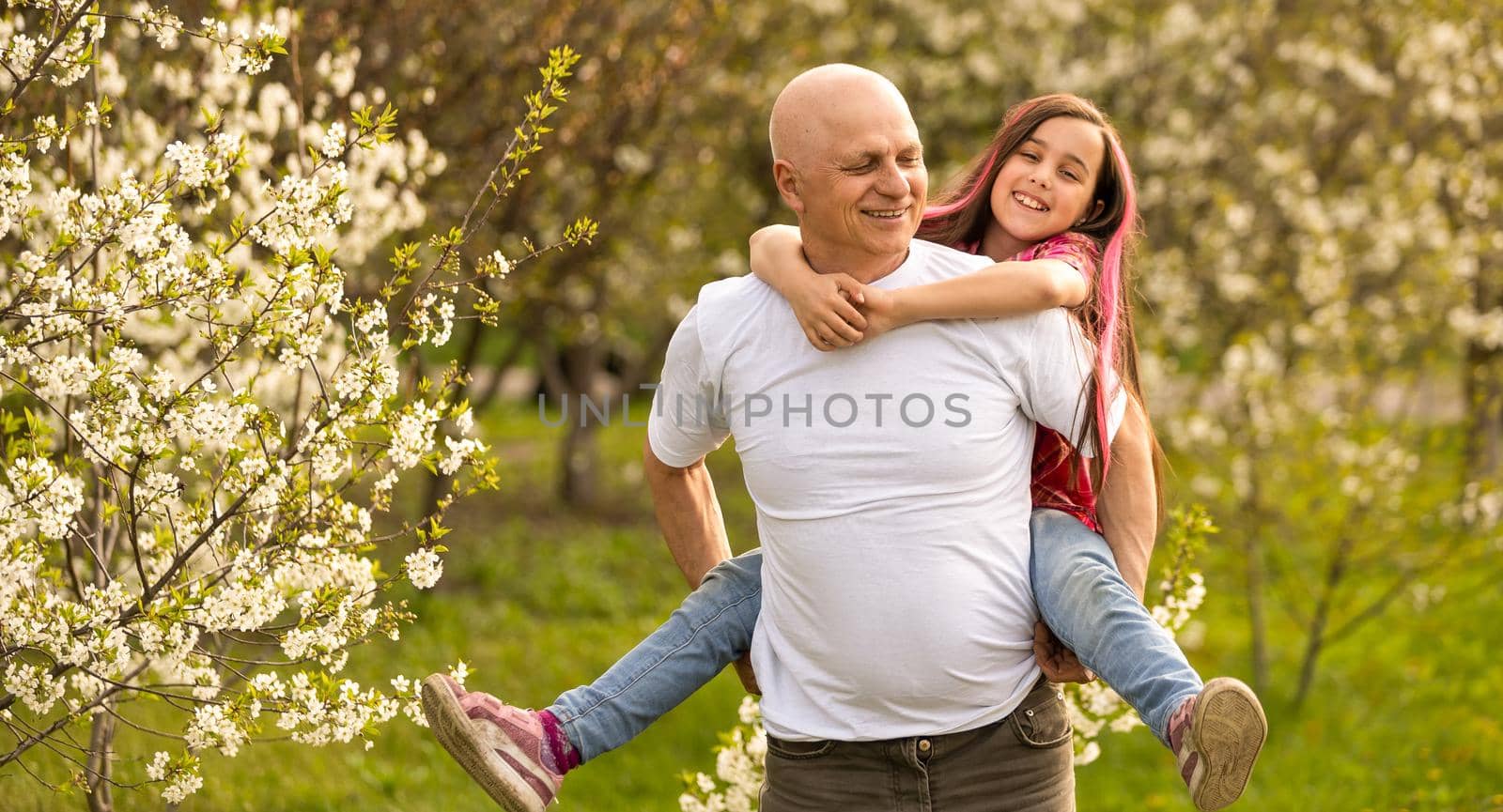 happy granddaughter hugging her smiling grandfather on green lawn.