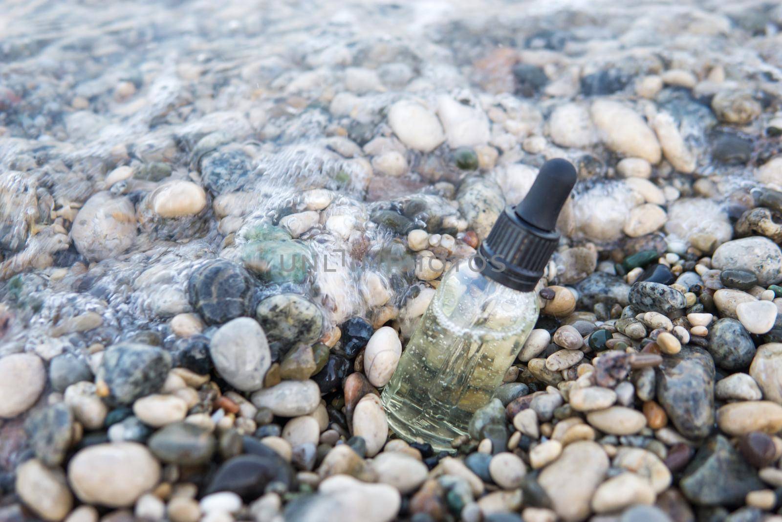 Cosmetic serum for the skin in a glass bottle. A bottle with an eyedropper on a pebble beach by the sea. Essences for skin care on the background of stones. The concept of natural cosmetics and SPA products.