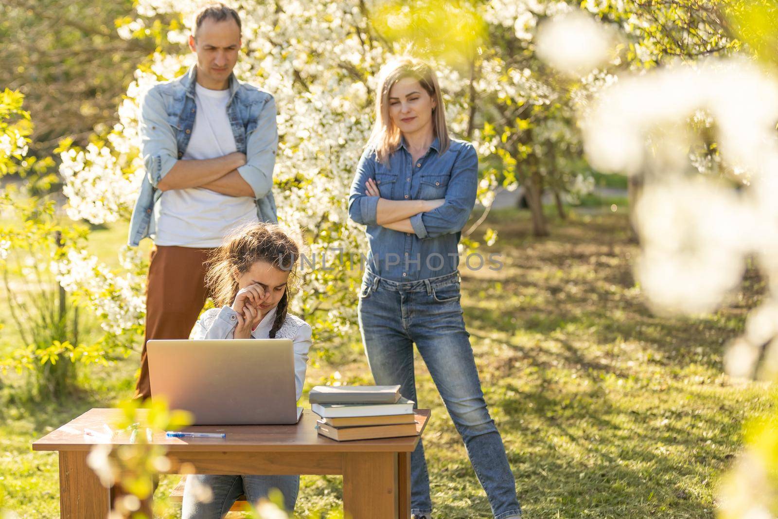 Happy family of four parents and cute little girl studying on laptop, enjoy using laptop watching cartoons, make internet video call or shopping online looking at computer screen sit together outdoor.