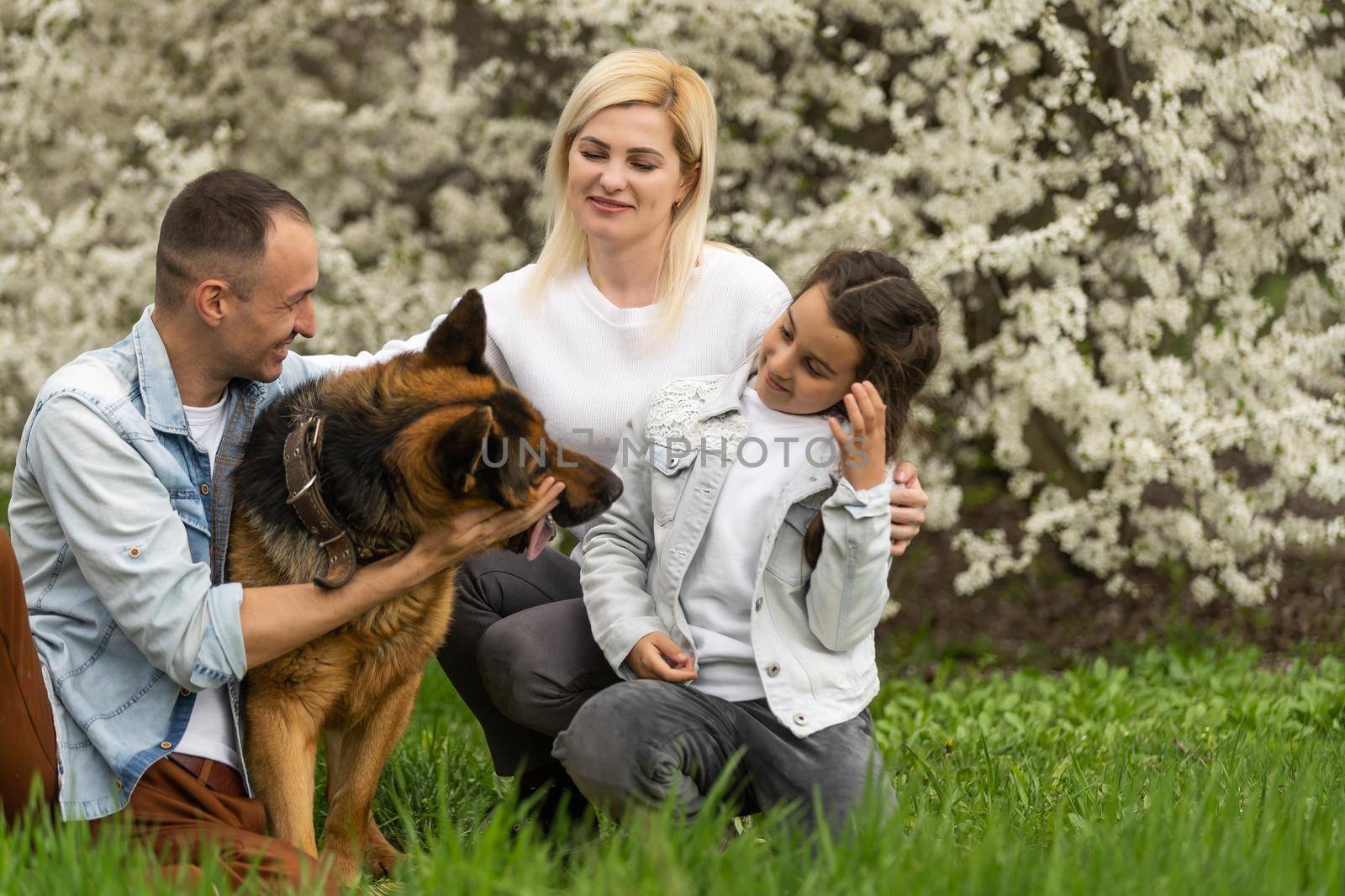 Outdoor portrait of happy young family playing in spring park under blooming tree, lovely family having fun in sunny garden.