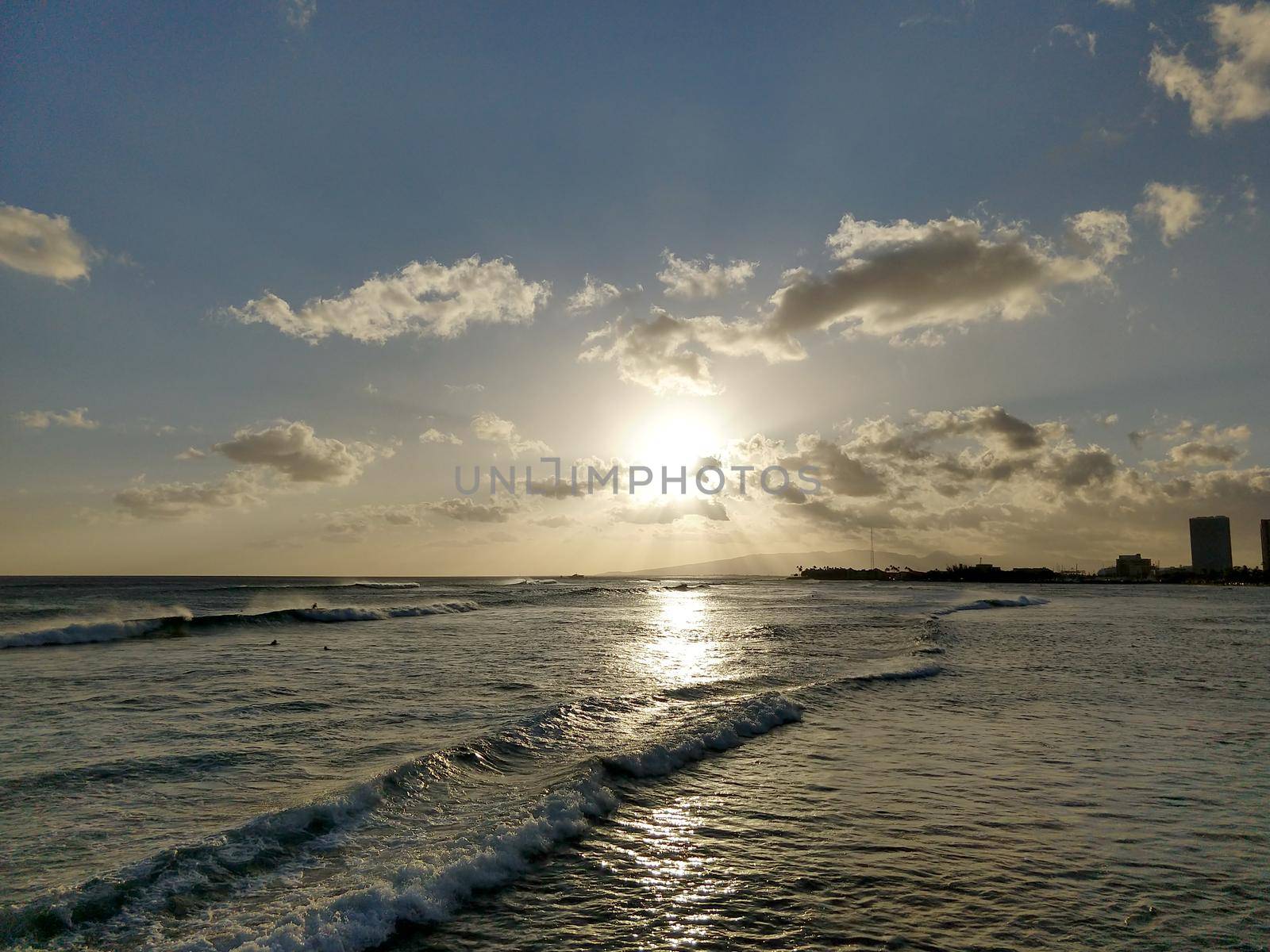 Sunset in the clouds on as wave lap towards the beach from the ocean at Ala Moana Beach Park on Oahu, Hawaii.