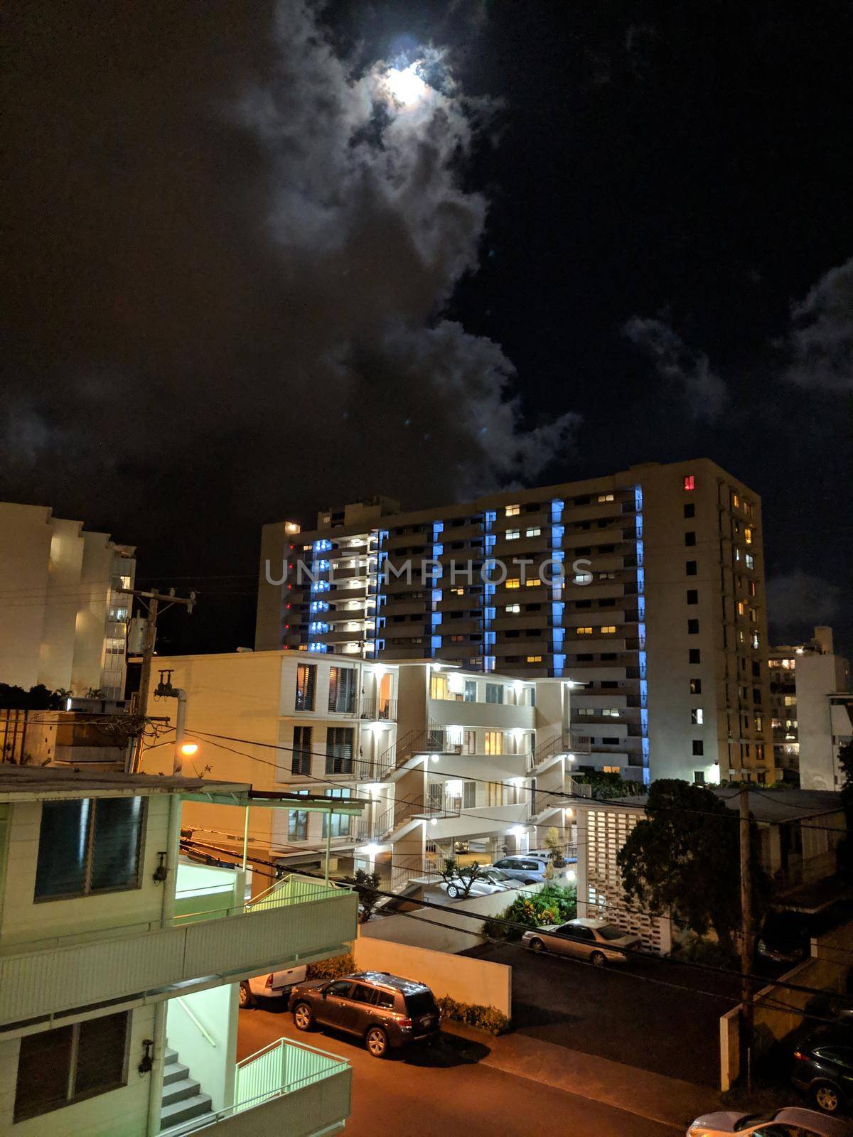 Full moon behind the clouds in Makiki, and Honolulu Cityscape high up during the evening with houses and modern highrises, and other small buildings.
