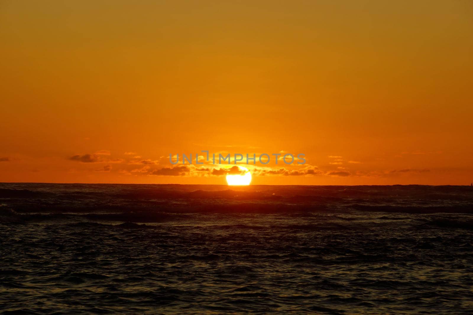 Sunset over the ocean through the clouds with light reflecting on ocean waves moving with boats on the water in the distance off Waikiki on Oahu, Hawaii.