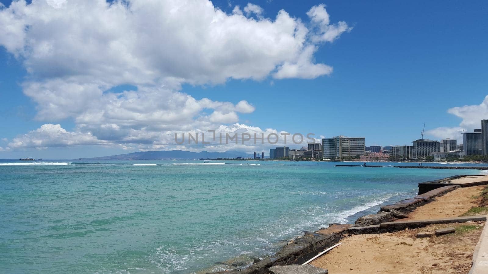 Beach in world famous tourist area Waikiki on a beautiful day with hotels in the distance and boats on the ocean.  