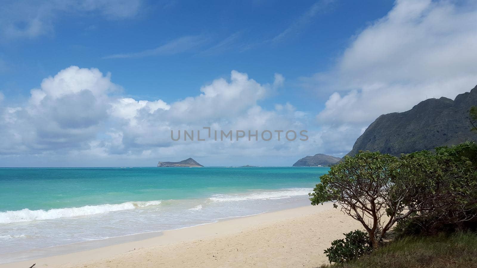 Gentle wave lap on Waimanalo Beach looking towards Rabbit island and Rock island on a nice day with clouds in the sky on Oahu, Hawaii. 