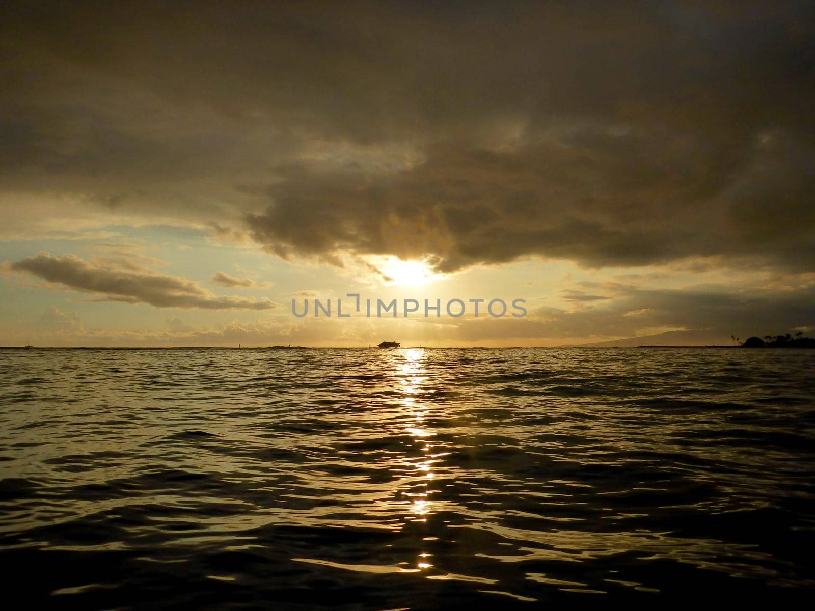 Sunset over the ocean with light reflecting on ocean waves moving with boats on the water in the distance off Waikiki with clouds on Oahu, Hawaii.