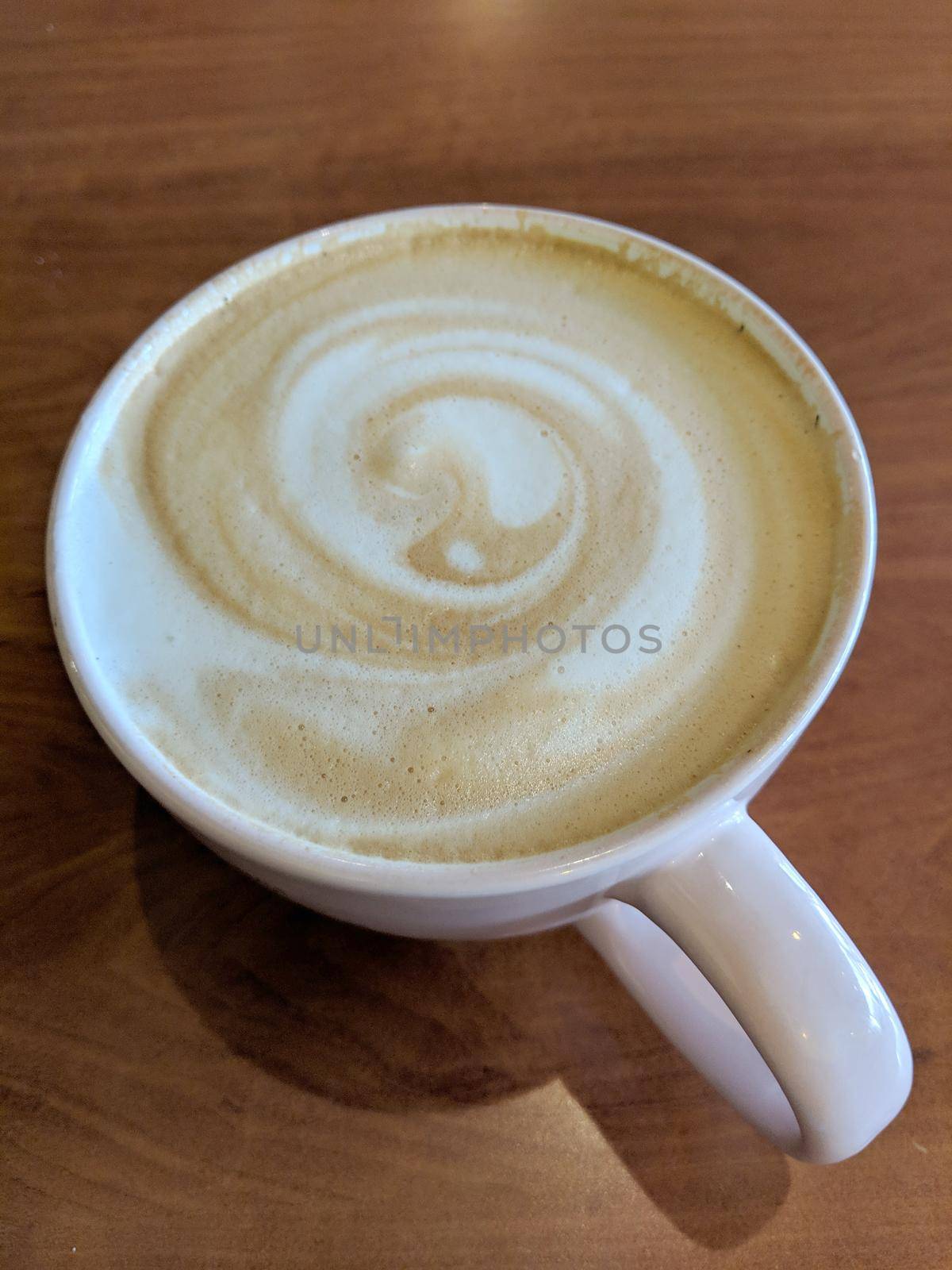White cup of Cappuccino with swirl in foam on saucer on table.