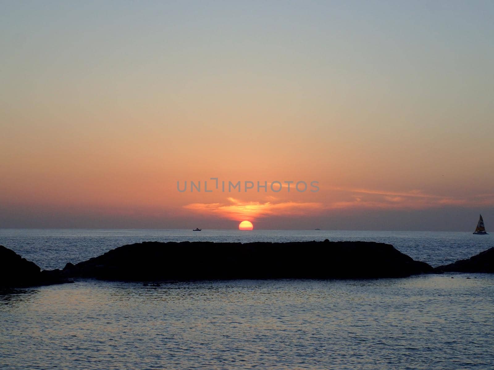 Sunsets behind the ocean with boats on the water and rock outcropping on Oahu, Hawaii.