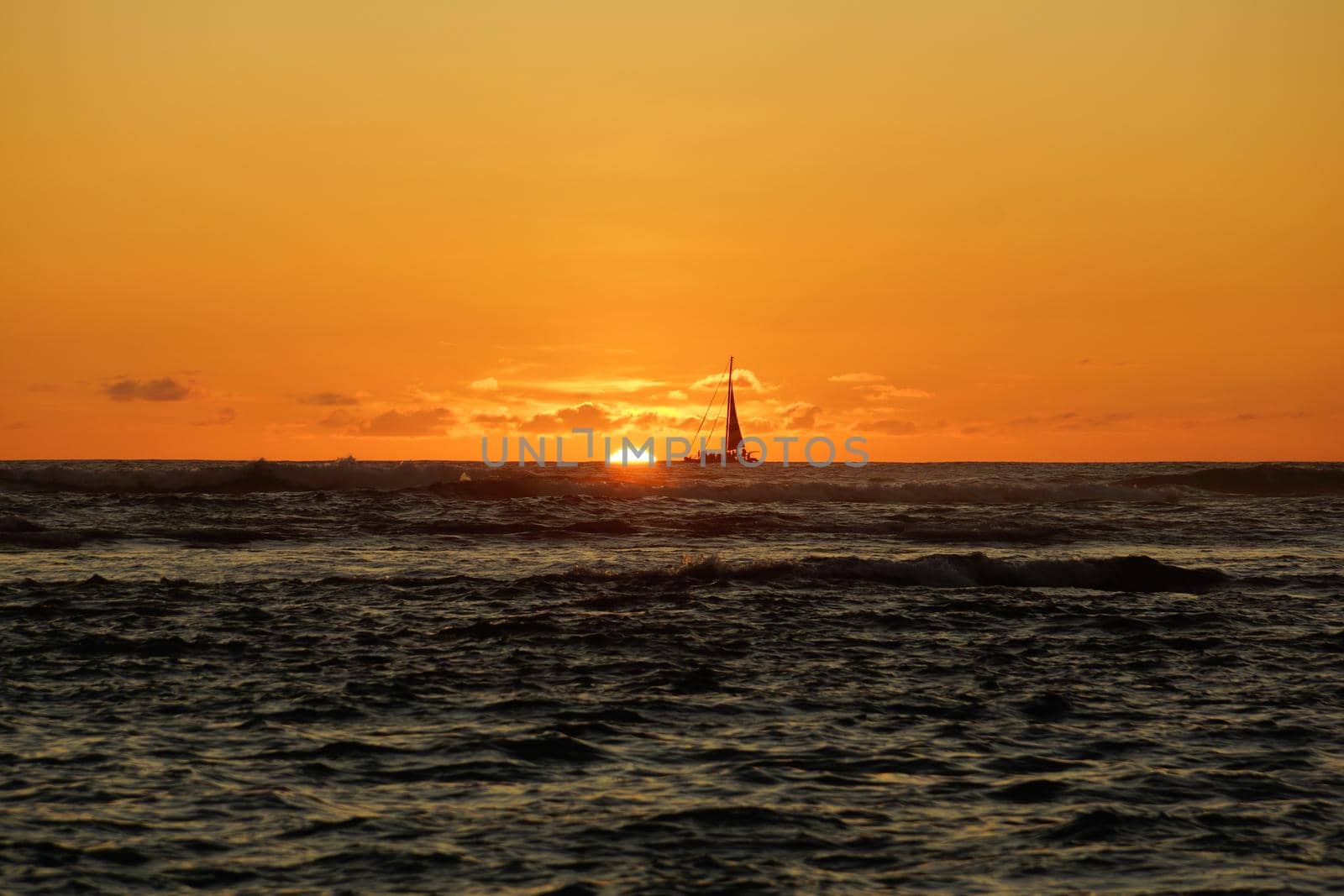 Sunset over the ocean with light reflecting on ocean waves moving with boats on the water in the distance off Waikiki with clouds on Oahu, Hawaii.