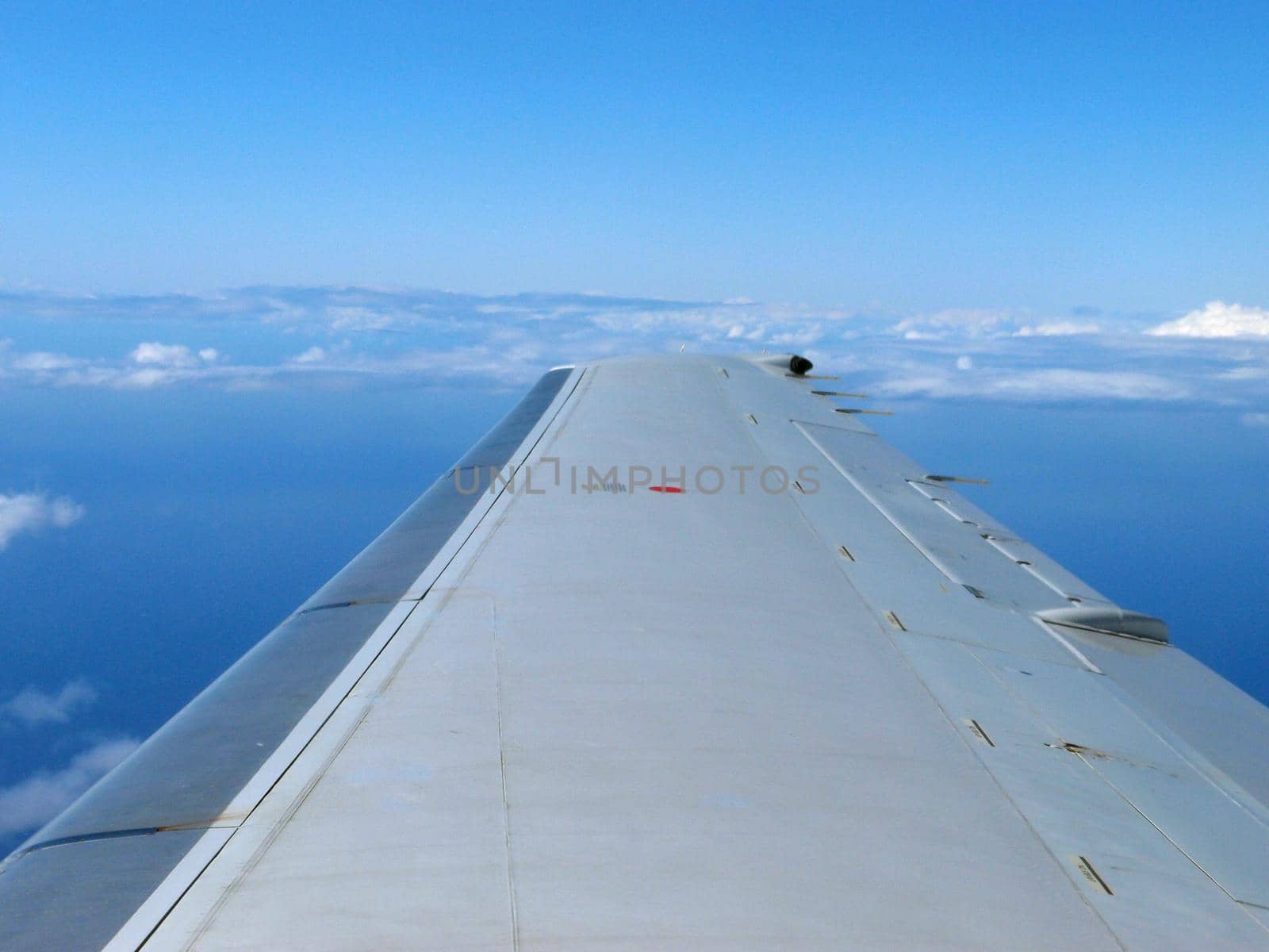 Aerial high in the sky, shot from above the clouds, with the wing of a commercial jet plane and blue skies.