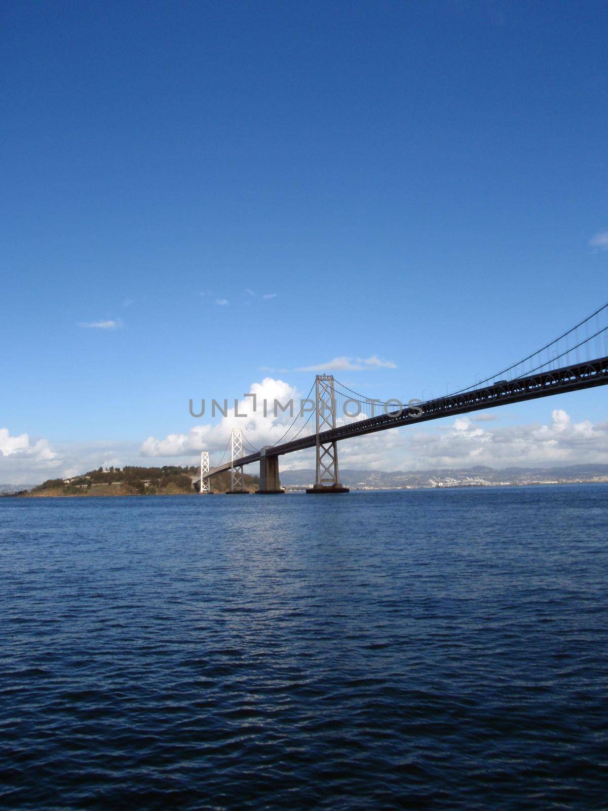 Cars cross the San Francisco side of Bay Bridge with Oakland in the distance on a clear day.