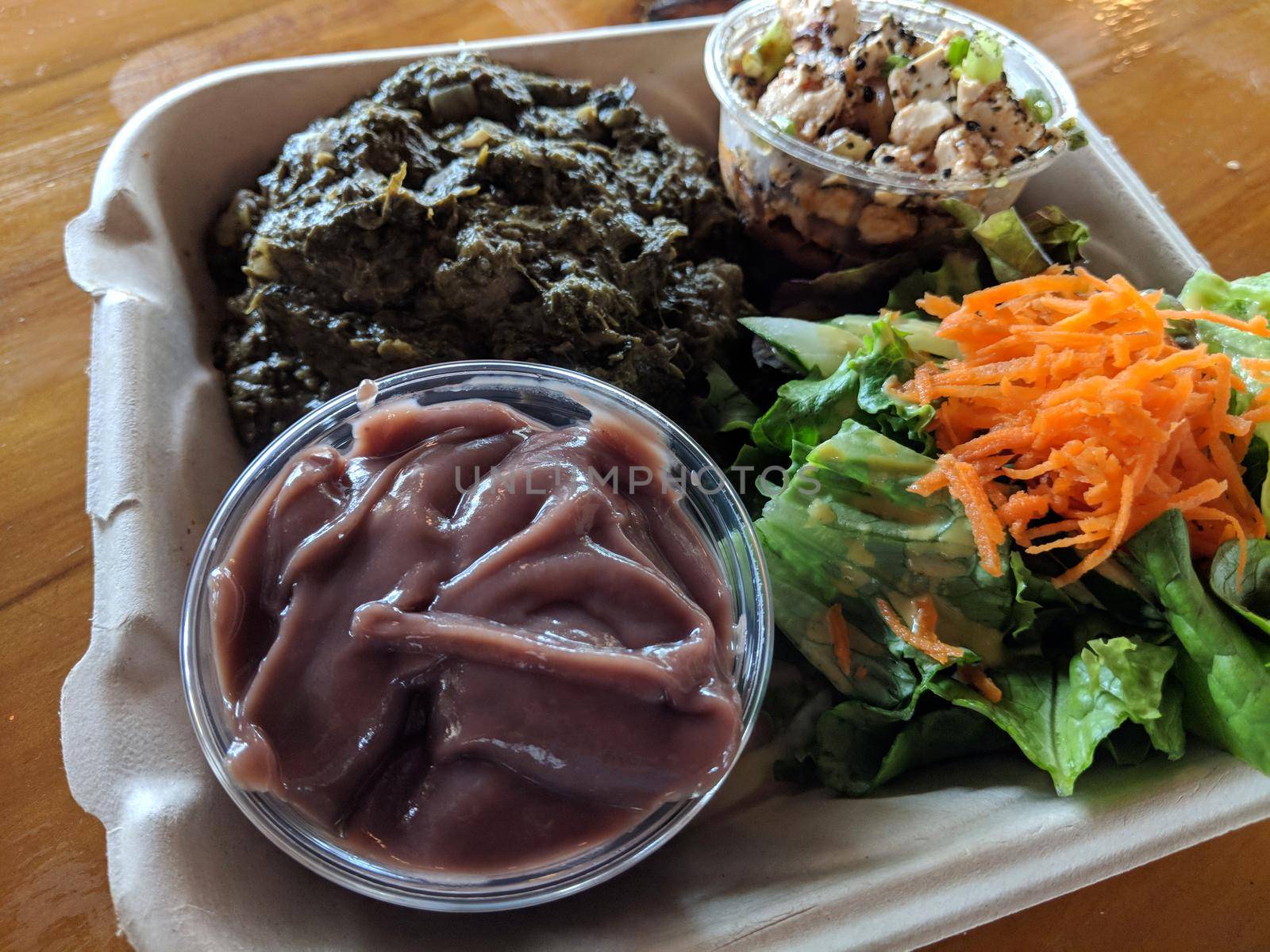 Hawaiian Lau Lau plate Served with Fresh/Day Old Poi in bowl, salad, Tofu poke in a cardboard container on a table.