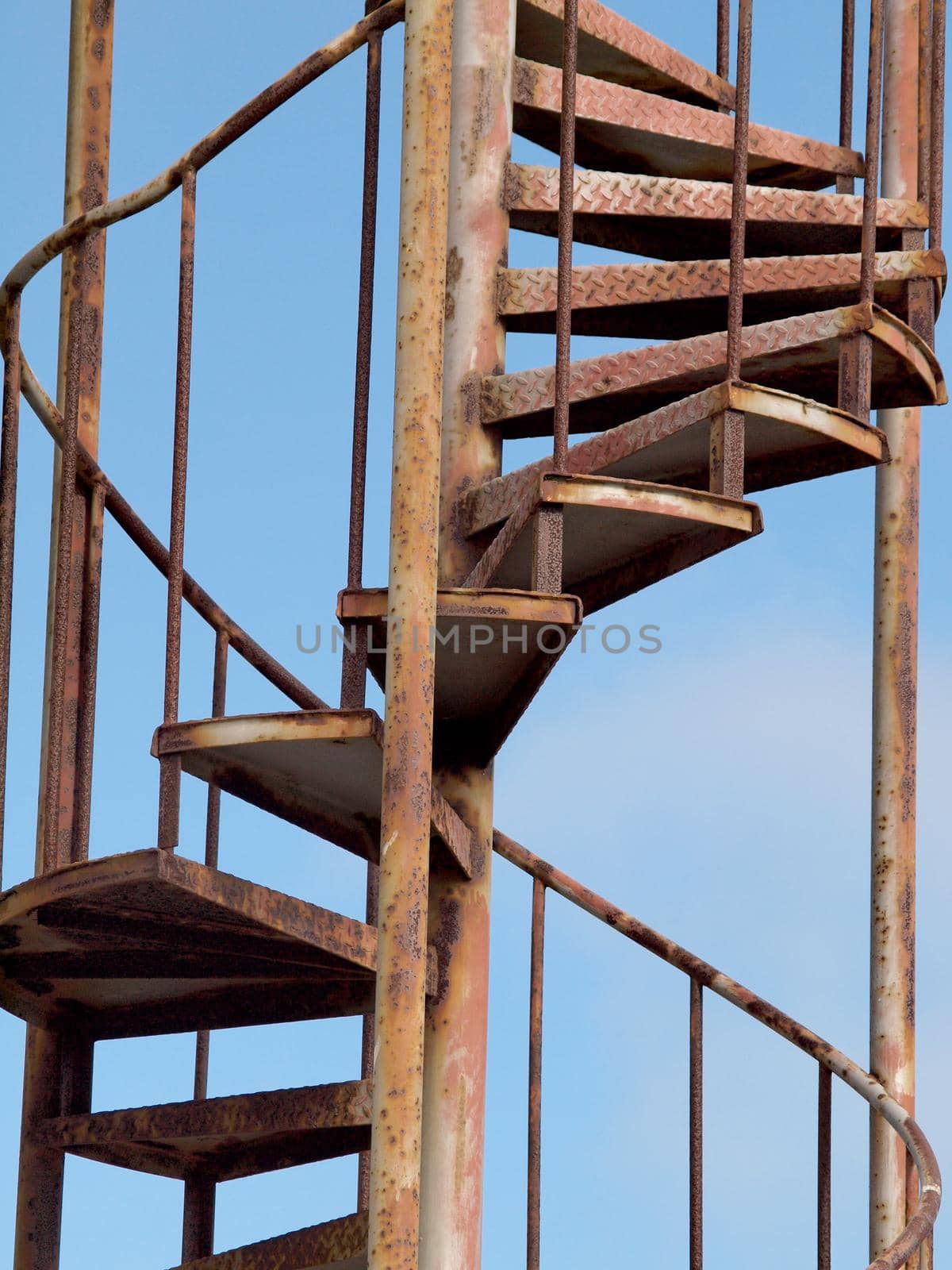 Old Rusted Metal Spiral Staircase against a blue sky.