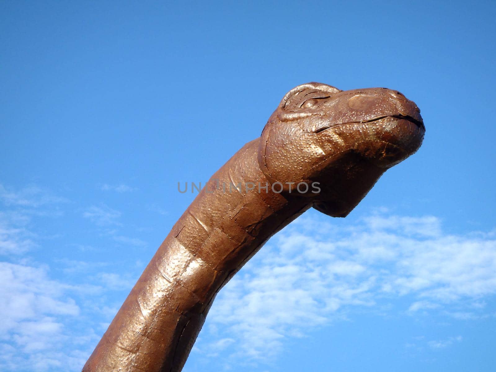 California - August 28, 2010: Metal Dinosaur Head and long Neck Brachiosaurus against a blue sky with clouds.