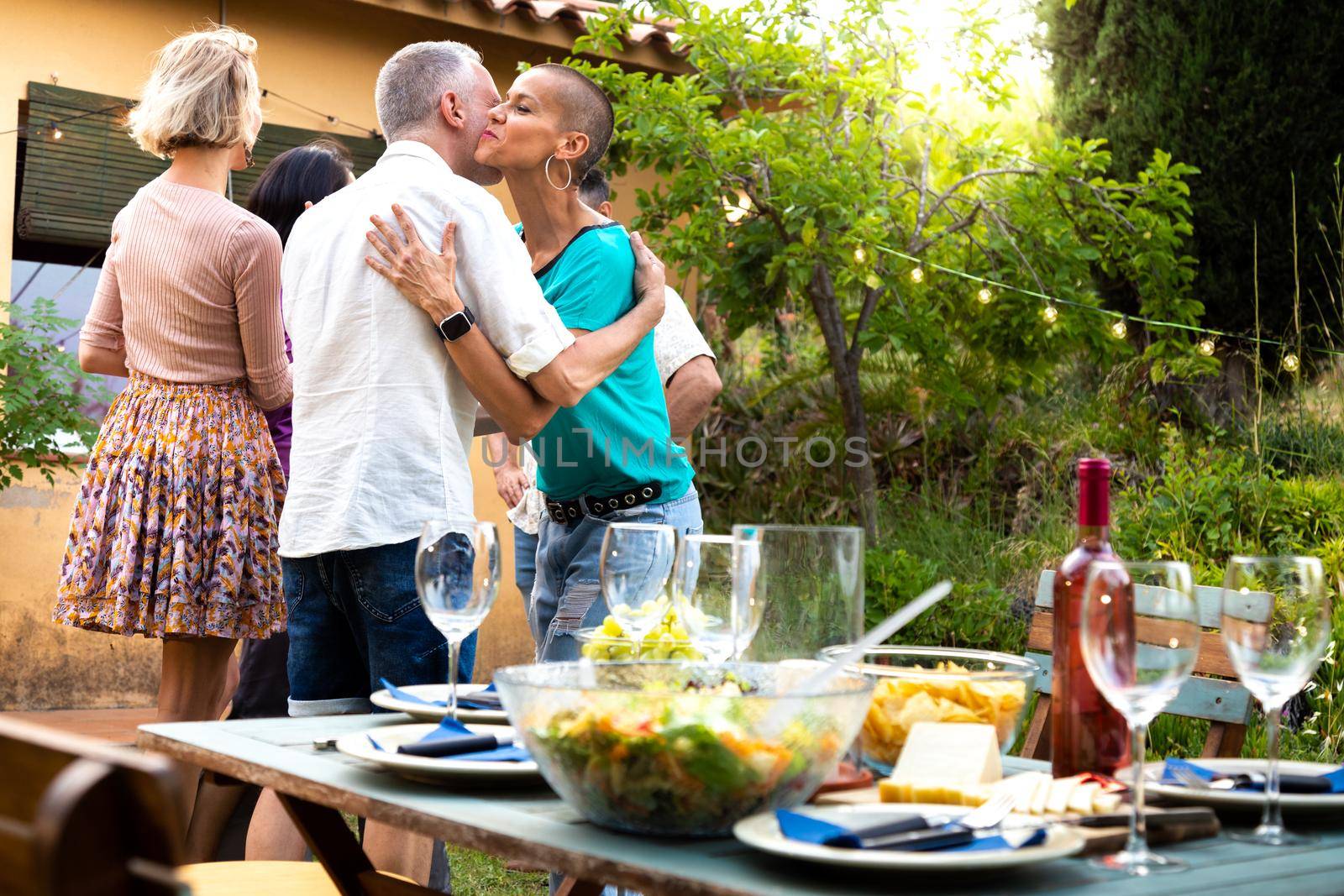 Friends arriving to garden dinner party. Hosts welcoming guests. by Hoverstock