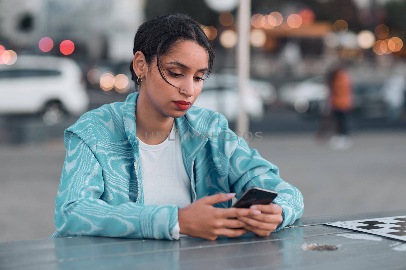 Sad, depressed and stressed female with mental health problem texting on phone while sitting at outdoor cafe. Young woman getting negative response or bad news while chatting or browsing social media by YuriArcurs