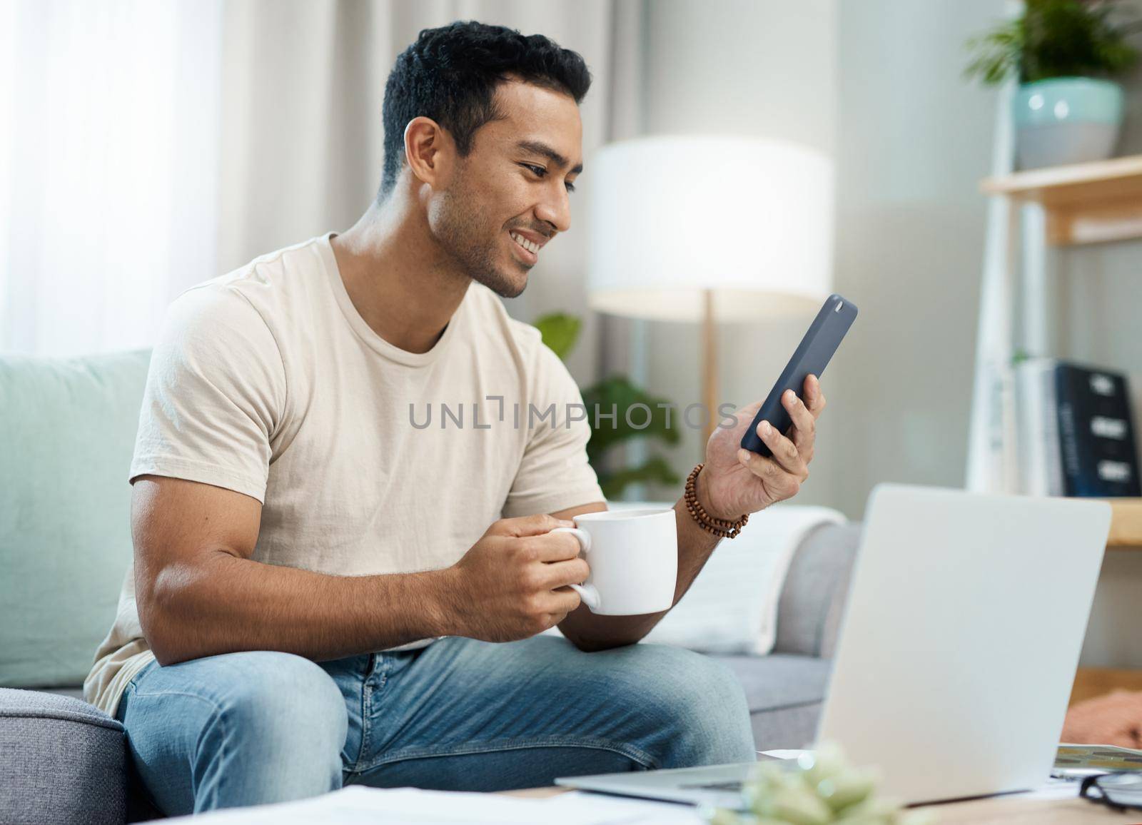 Coffee and technology go hand-in-hand. a young man sitting in his living room and using technology while enjoying a cup of coffee. by YuriArcurs