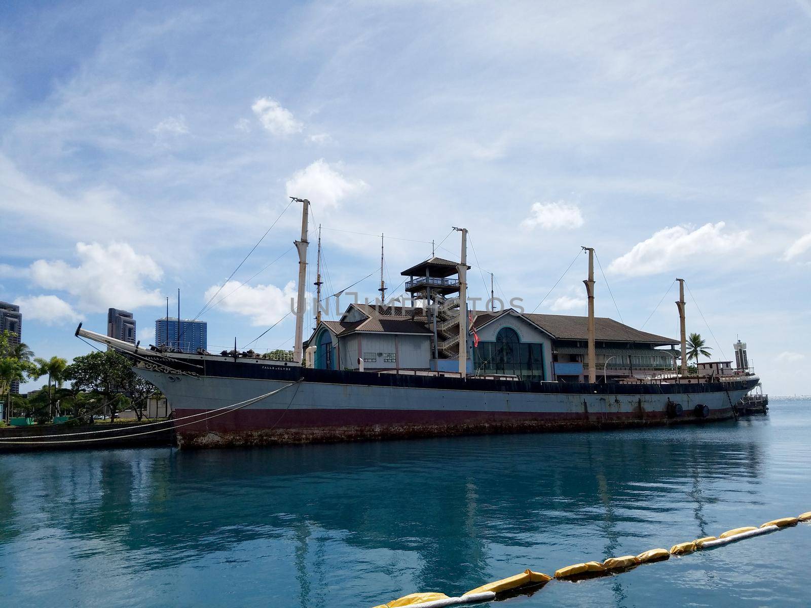 Historic Falls of Clyde Ship sits in Honolulu Harbor during the day. Falls of Clyde is the last surviving iron-hulled, four-masted full rigged ship, and the only remaining sail-driven oil tanker built in the 19th century. Designated a U.S. National Historic Landmark in 1989