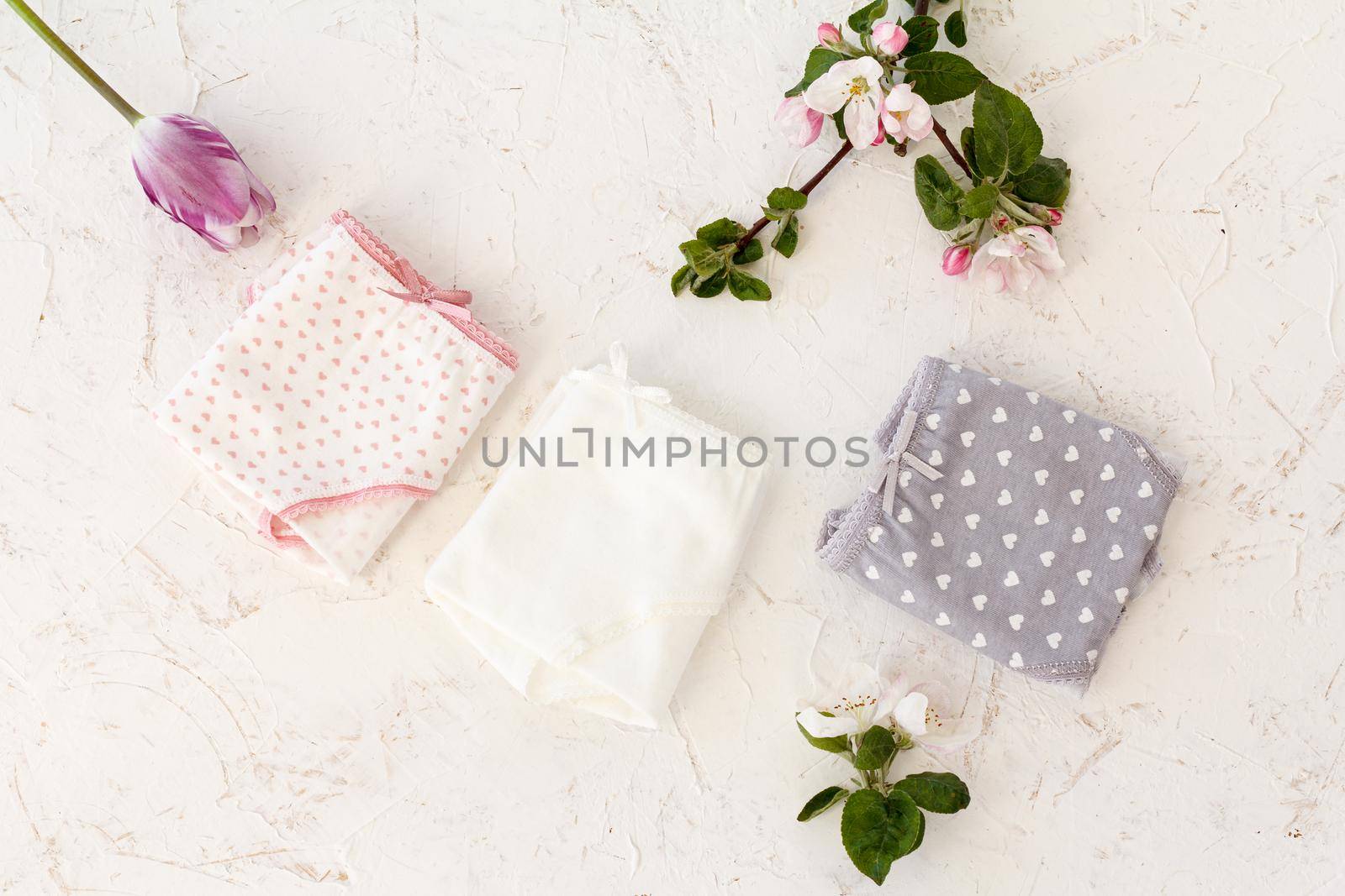 Folded cotton panties of different color with a tulip and flowers of an apple tree on the white background. Woman underwear set. Top view.