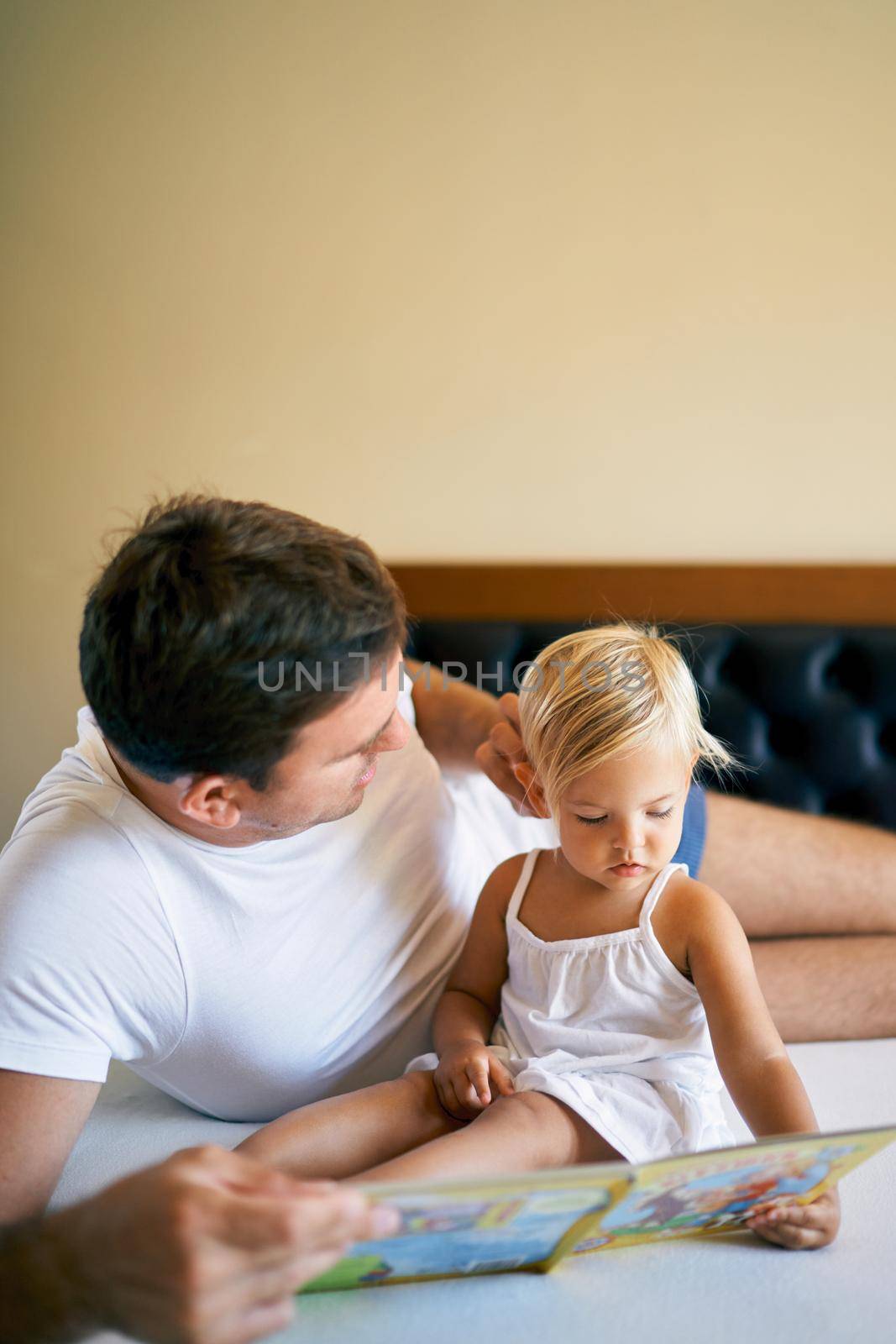 Dad straightens hair of little daughter reading a book by Nadtochiy