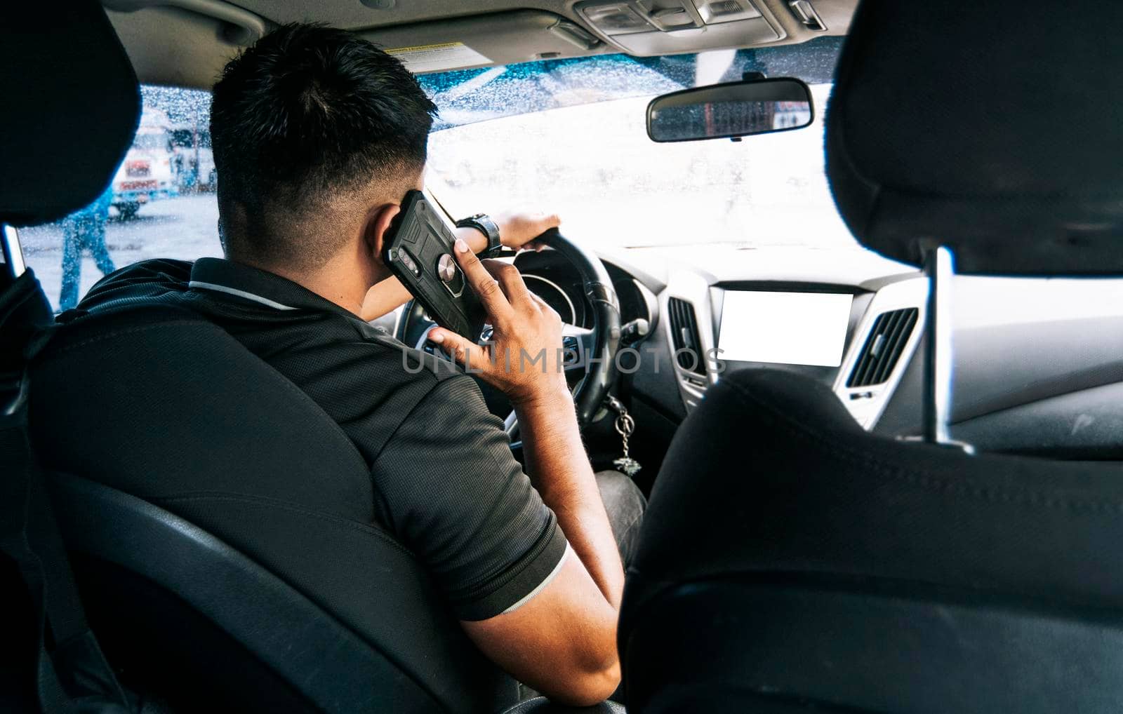 Man driver calling on the phone in his car, Back view of a young man sitting inside car using mobile phone, concept of man calling on the phone while driving by isaiphoto