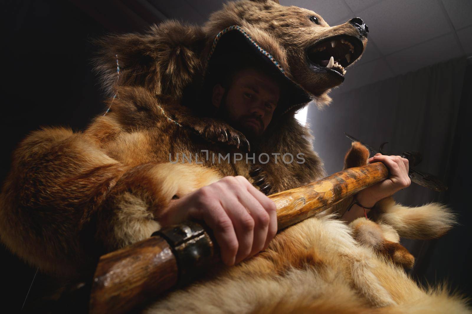 bearded serious man sits in a suit in the skin of a dead bear with an ax in his hands.