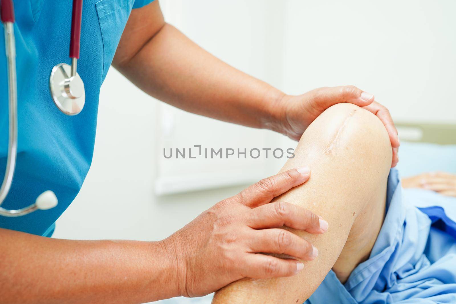 Doctor checking Asian elderly woman patient with scar knee replacement surgery in hospital.