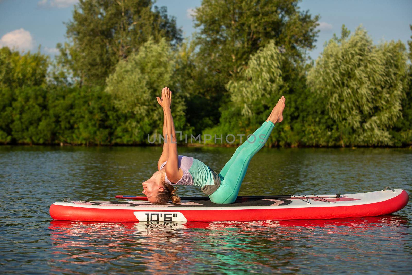 Young woman doing yoga on sup board with paddle. Yoga pose, side view - concept of harmony with the nature. by nazarovsergey