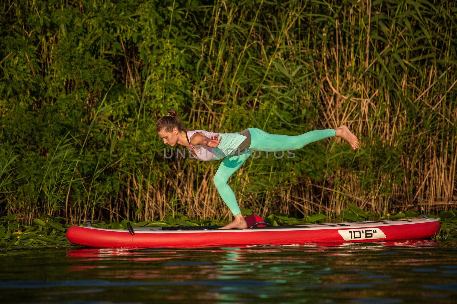 Young woman are doing yoga on a stand up paddle board SUP on a beautiful lake or river. The concept of a healthy lifestyle. Sport. Yoga. Hobby