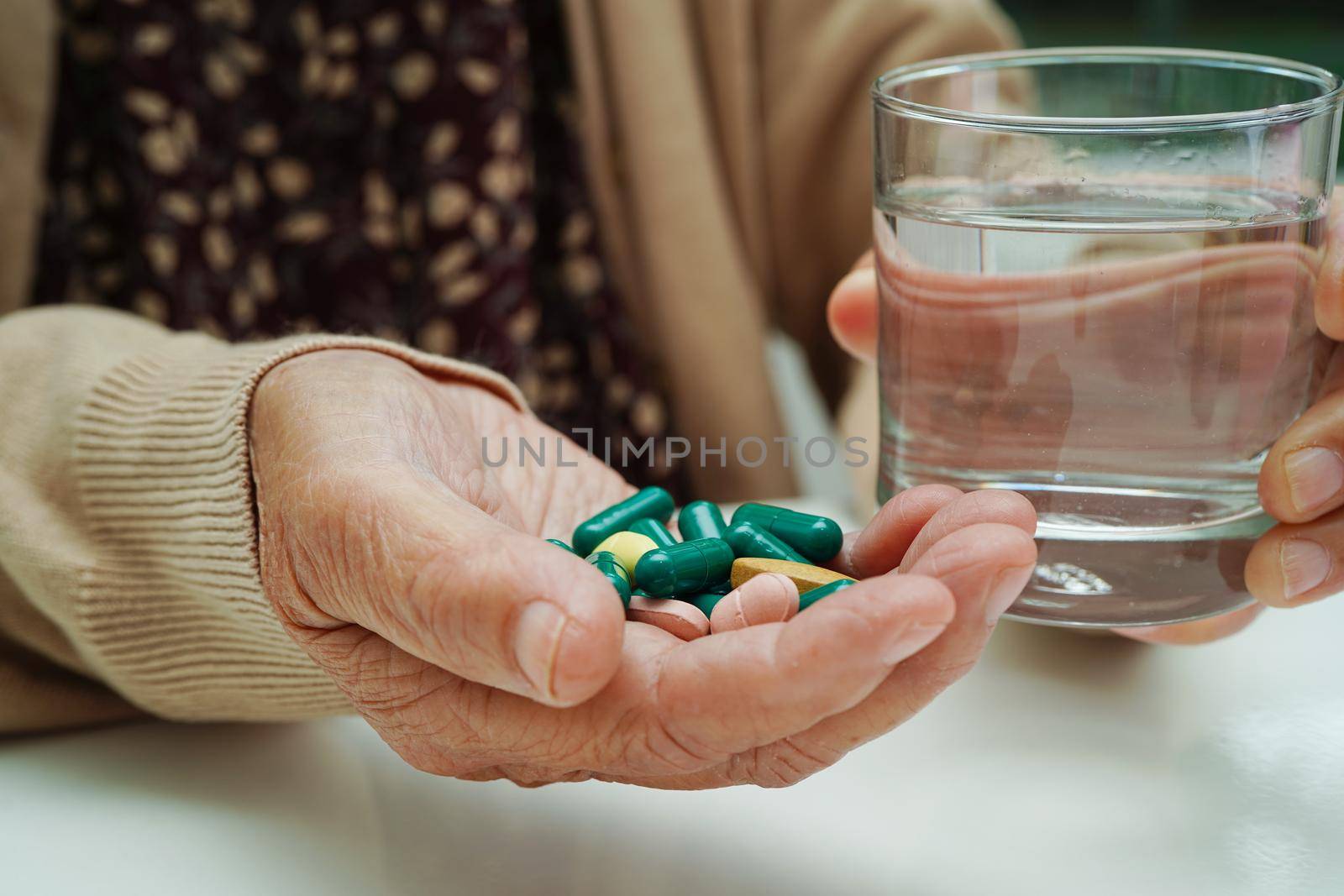 Asian elderly woman holding pill drug with water in glass, strong healthy medical concept.