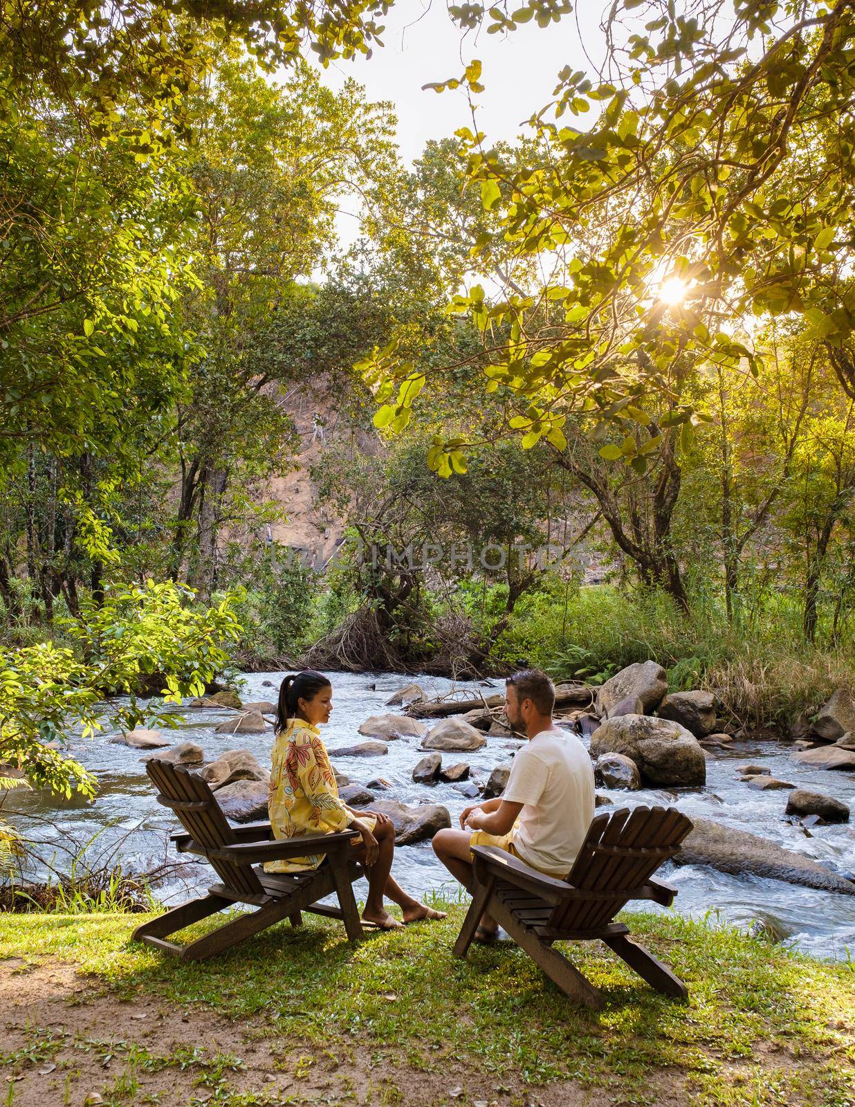 a couple of men and women relaxing by a streaming river in a chair, camping in nature concept. Asian women and Caucasian men on vacation in South Africa