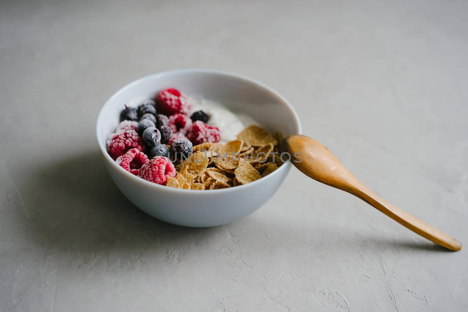 Healthy breakfast with berries, cereals and natural yogurt. Multi-lacquered cereals for breakfast. Berries in ice. Frozen raspberries and black currants. Wooden spoon. Delicious and healthy breakfast.
