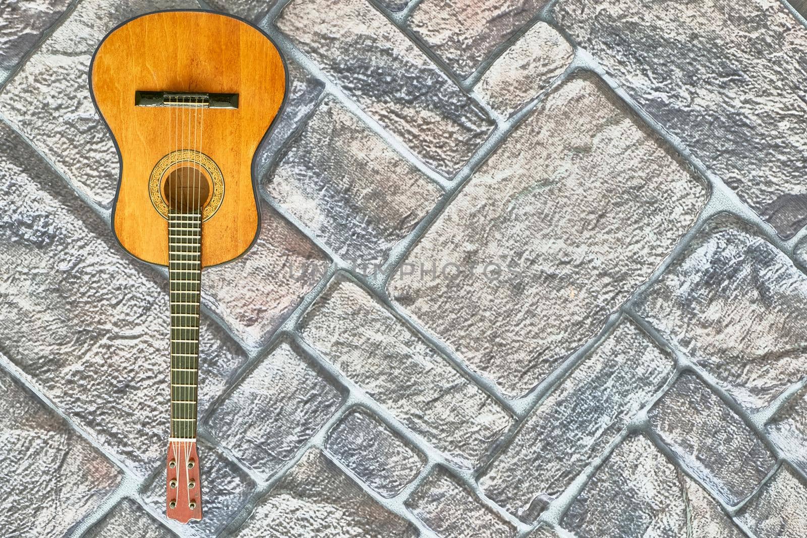 Yellow orange acoustic guitar on gray brown brick wall by jovani68