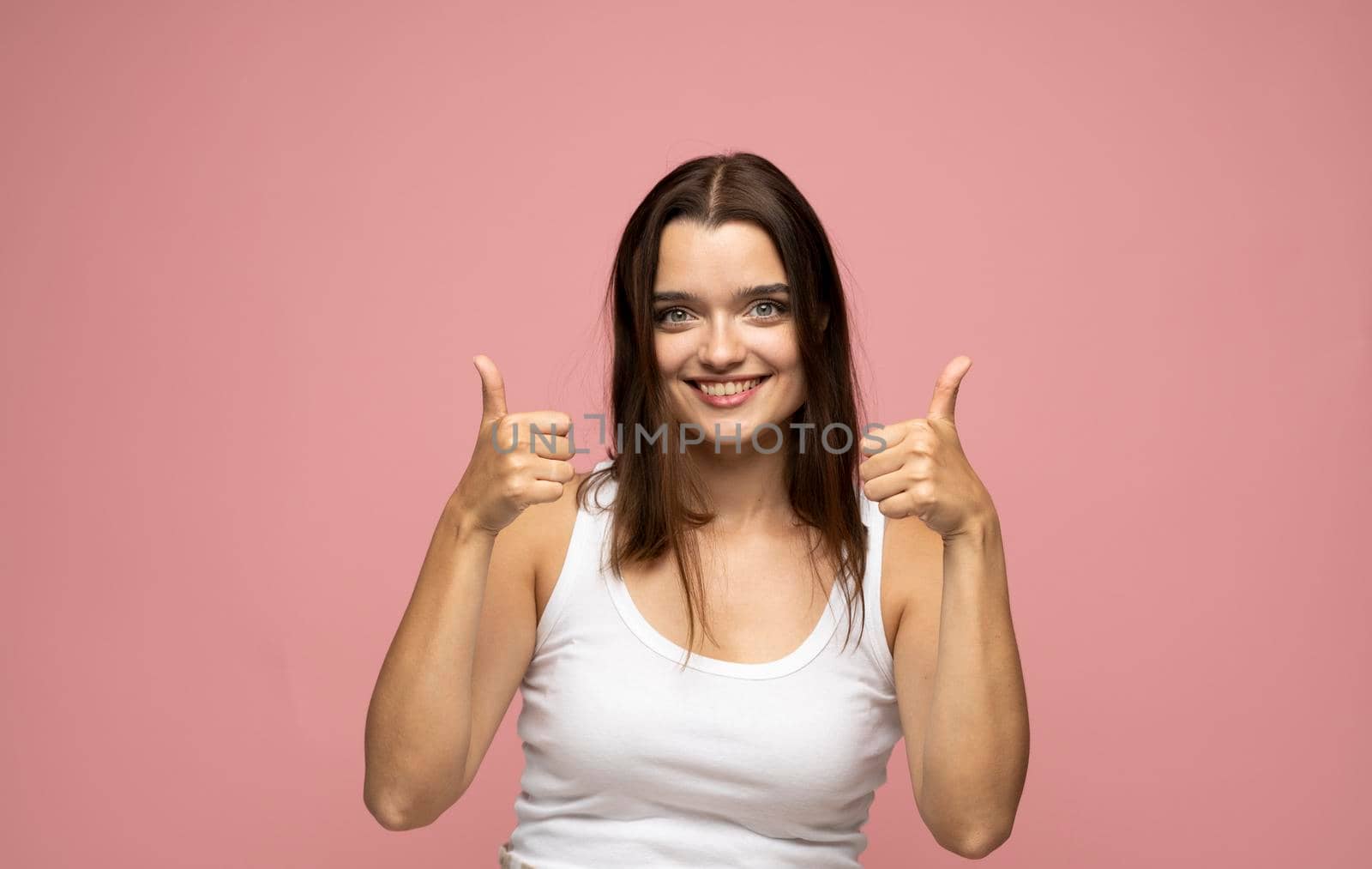 Happy young brunette female wearing white t-shirt making thumb up sign and smiling cheerfully, showing her support and respect to someone. I like that. Good job. by vovsht