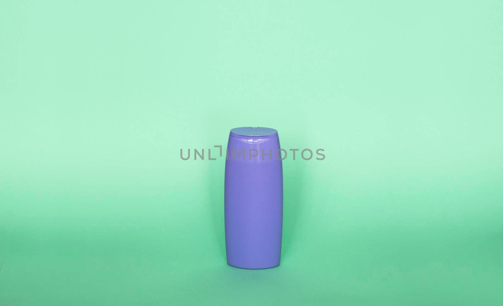 Violet plastic bottle of body care and beauty products. Studio photography of plastic bottle for shampoo, shower gel, creme isolated on green background