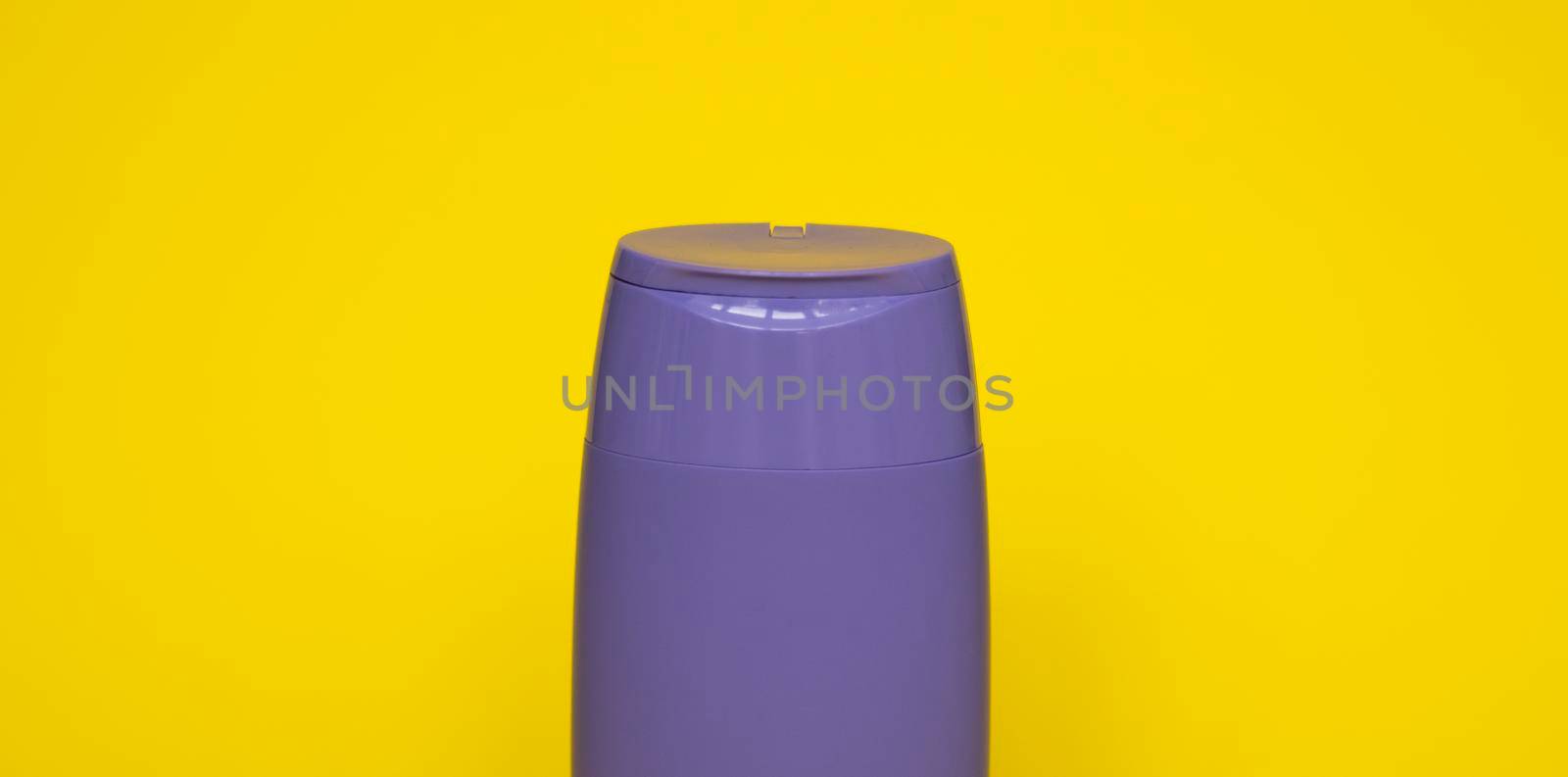 Violet plastic bottle of body care and beauty products. Studio photography of plastic bottle for shampoo, shower gel, creme isolated on yellow background