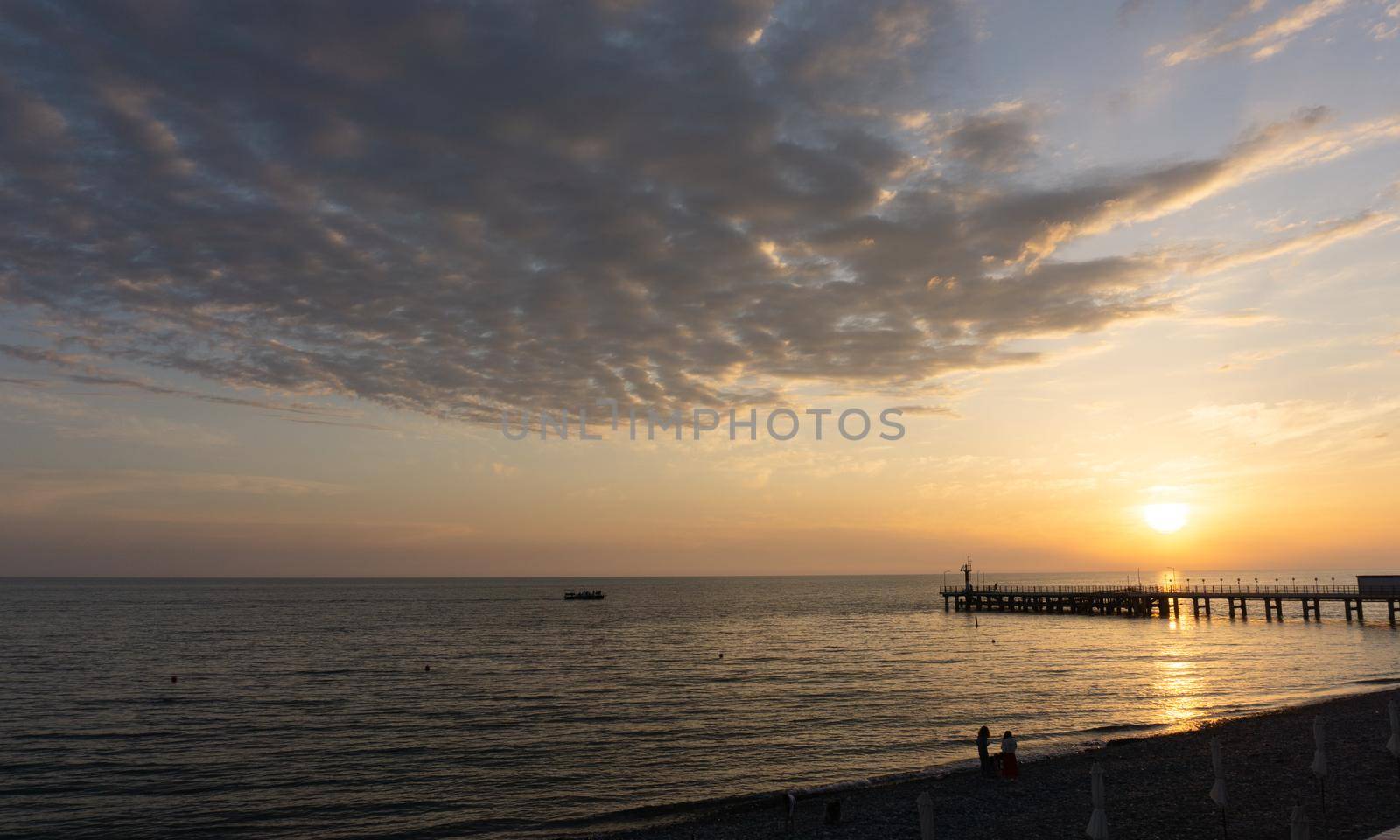 LAZAREVSKOE, SOCHI, RUSSIA - MAY, 26, 2021: Orange saturated sunset with silhouettes of people on the background of the sun. Lazarevskoe, Sochi, Russia by Asnia