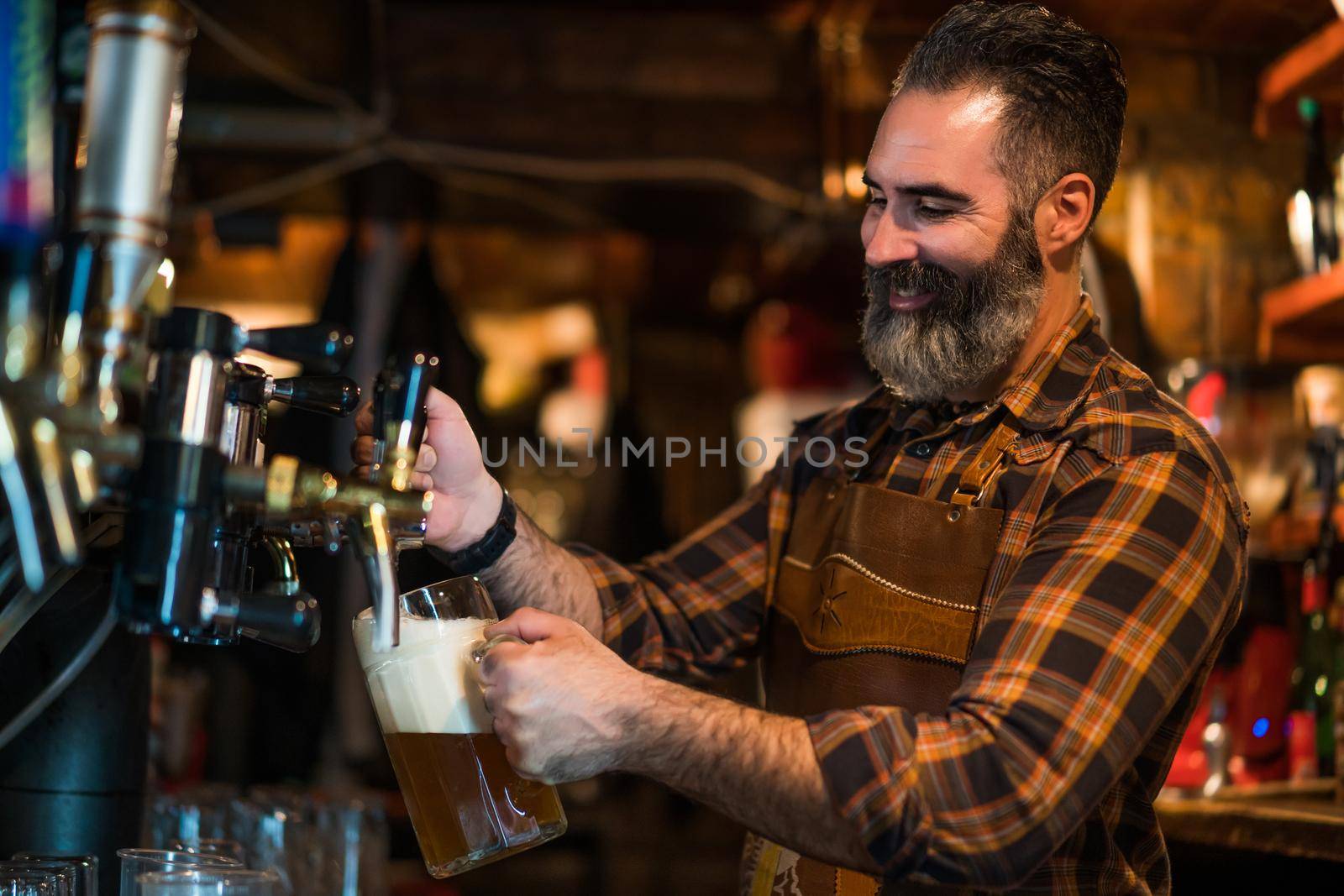 Portrait of cheerful barmen at pub. He pours beer into a beer glass.