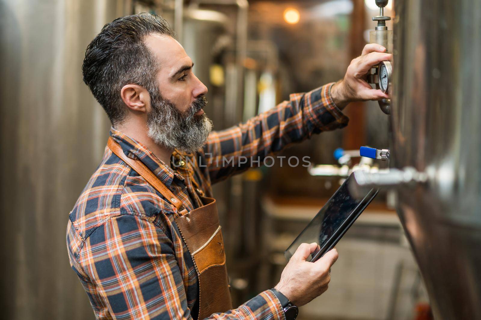 Man is working at craft beer factory. He is operating machinery in brewery. Small family business, production of craft beer.